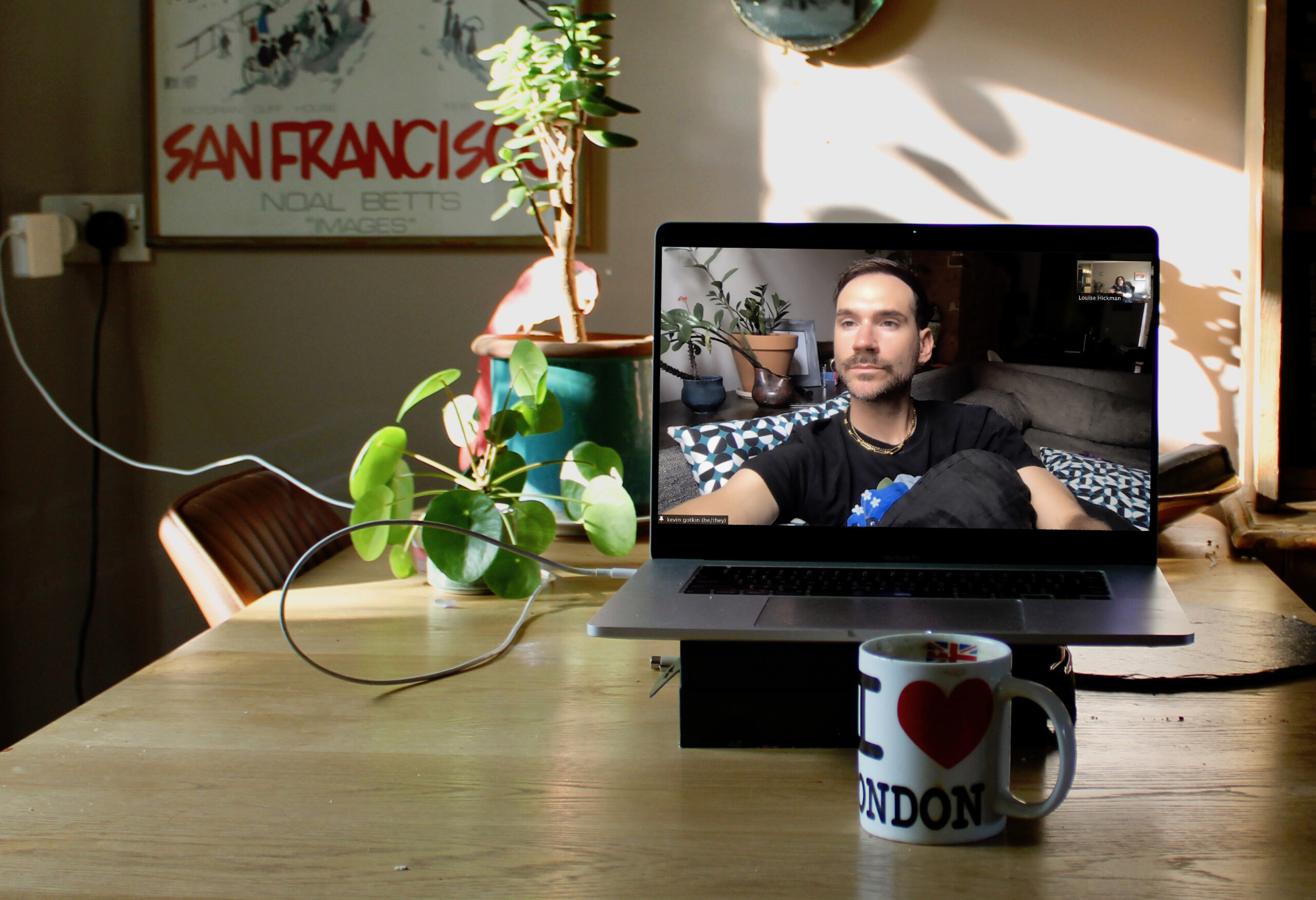 Kevin is in two places at once. They are on their couch, buoyed by pillows, looking past the camera. They are a scruffy white person with short brown hair. They...