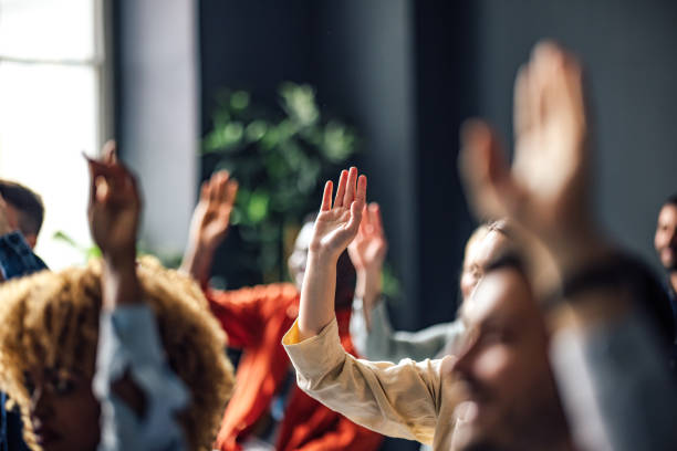 Group Of People Sitting On A Seminar. They Have Their Hand Raised.