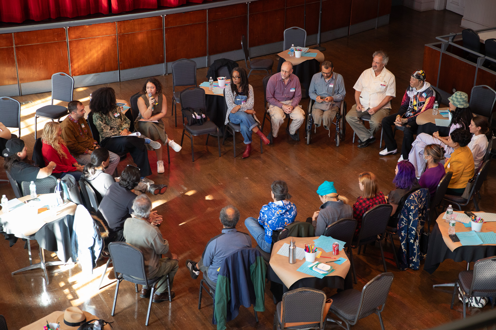 An aerial view of a large circle of people, all seated in a large room and in conversation with one another.
