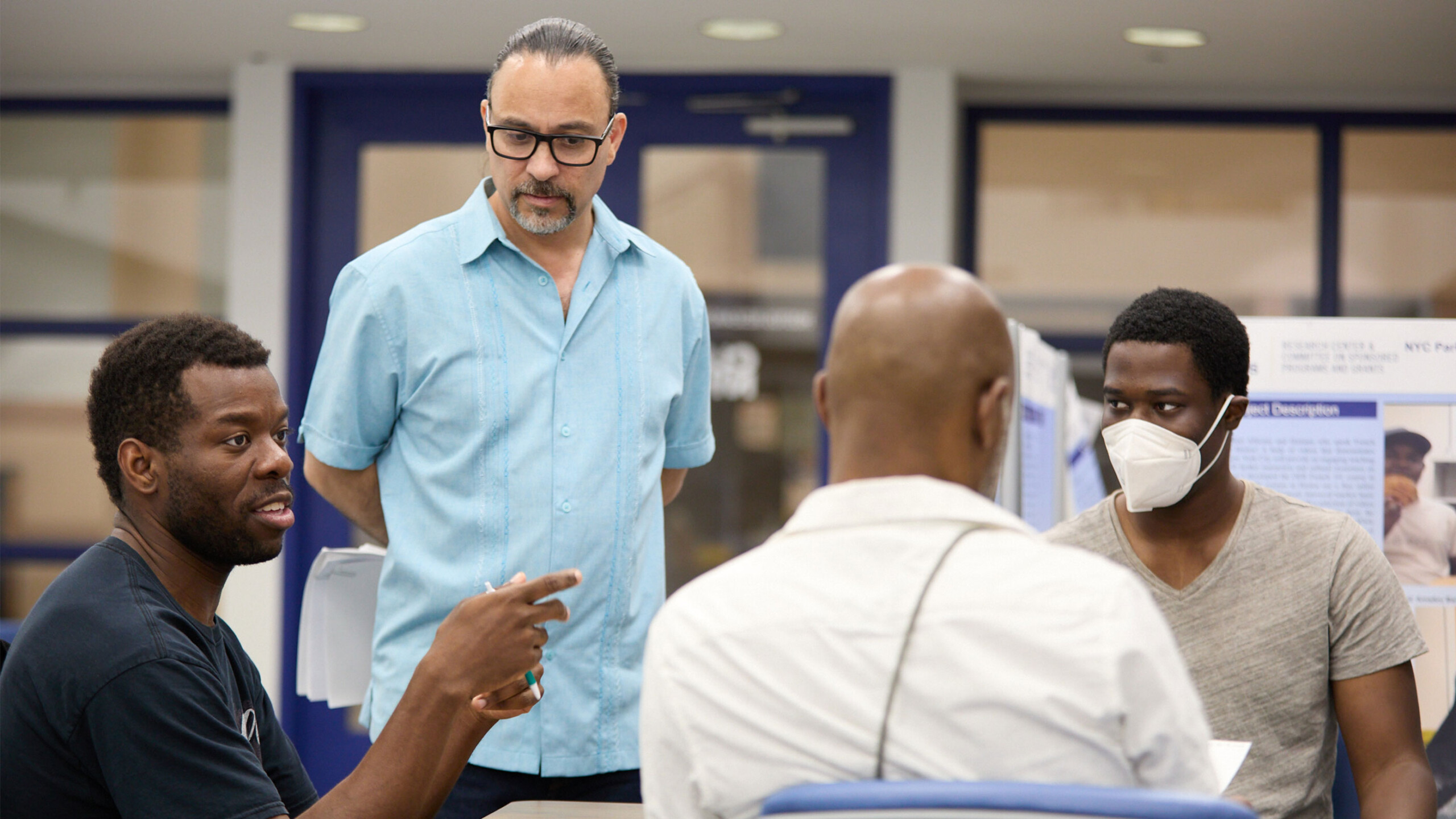 Individuals engaged in discussion near informational posters at an indoor event.