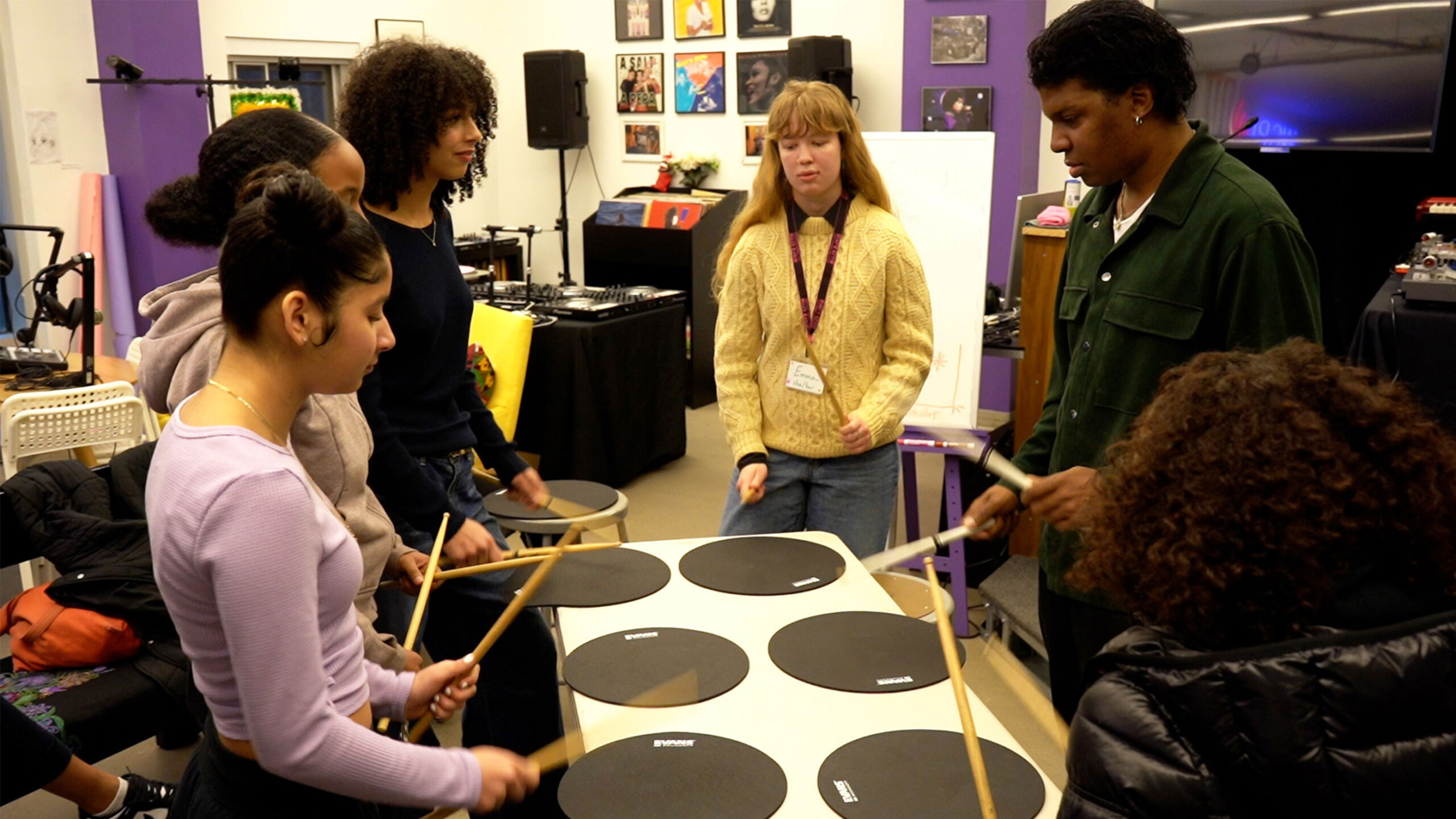 Group of people engaged in a drumming session on practice pads in a music room.