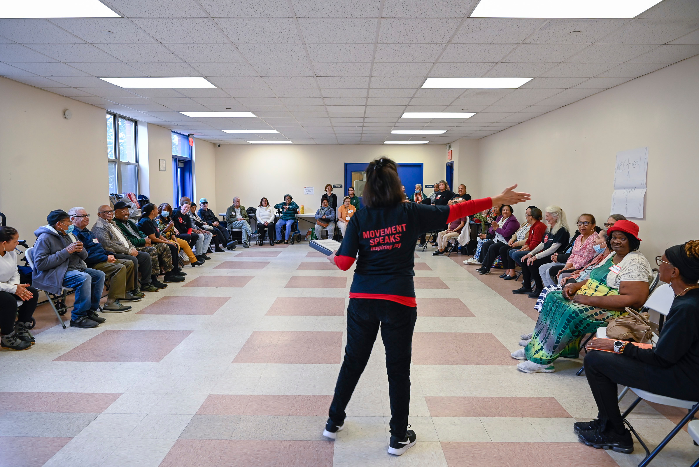 A speaker addresses a seated audience in a community hall.