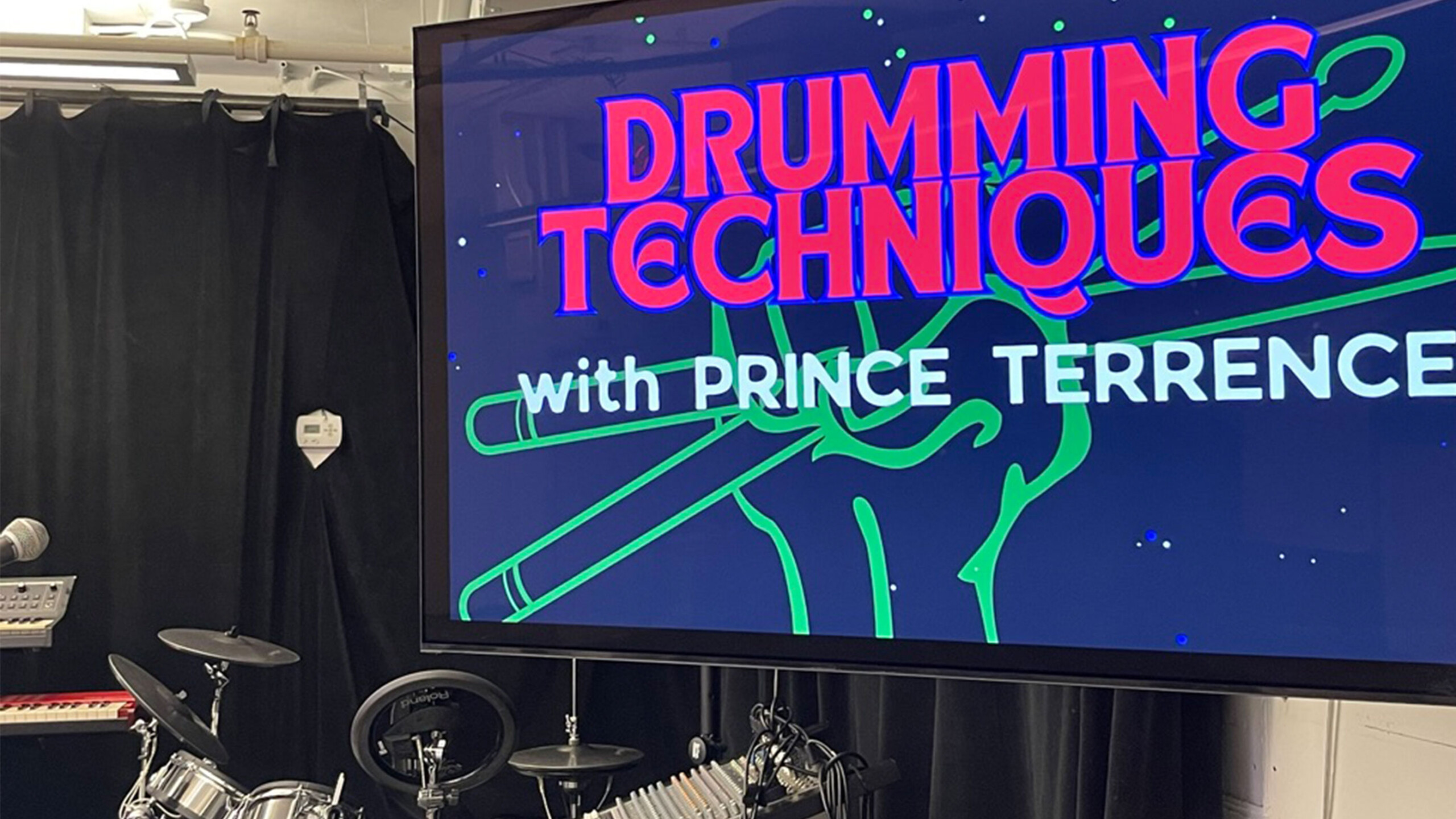 A drum set in front of a screen displaying DRUMMING TECHNIQUES with PRINCE TERRENCE.