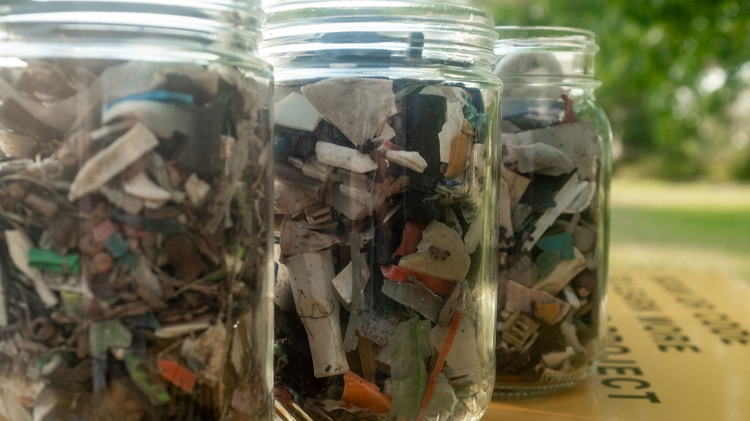 Three glass jars filled with assorted microplastics on a blurred background.