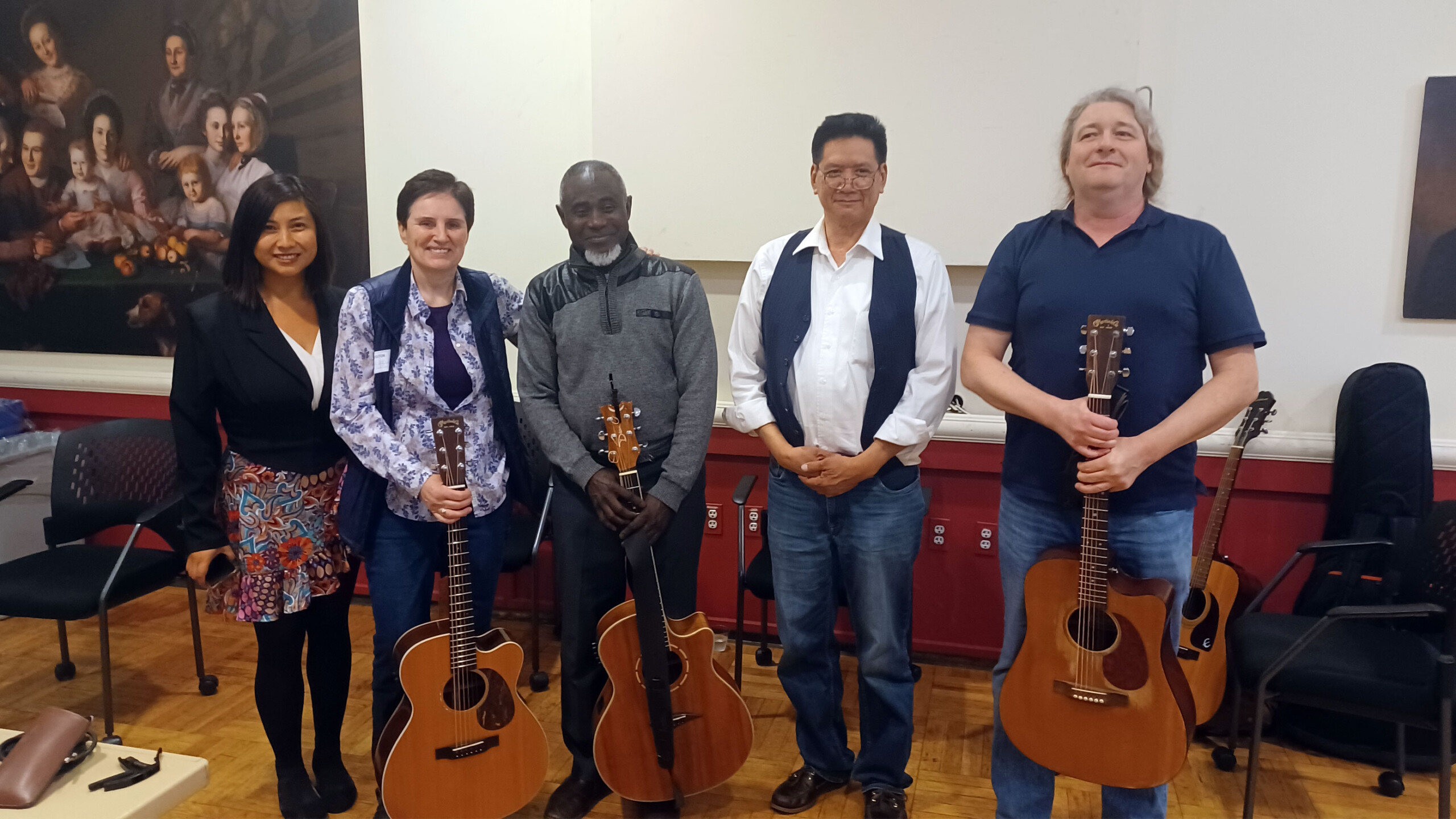 Group of musicians holding acoustic guitars in a room with classical painting in the background.