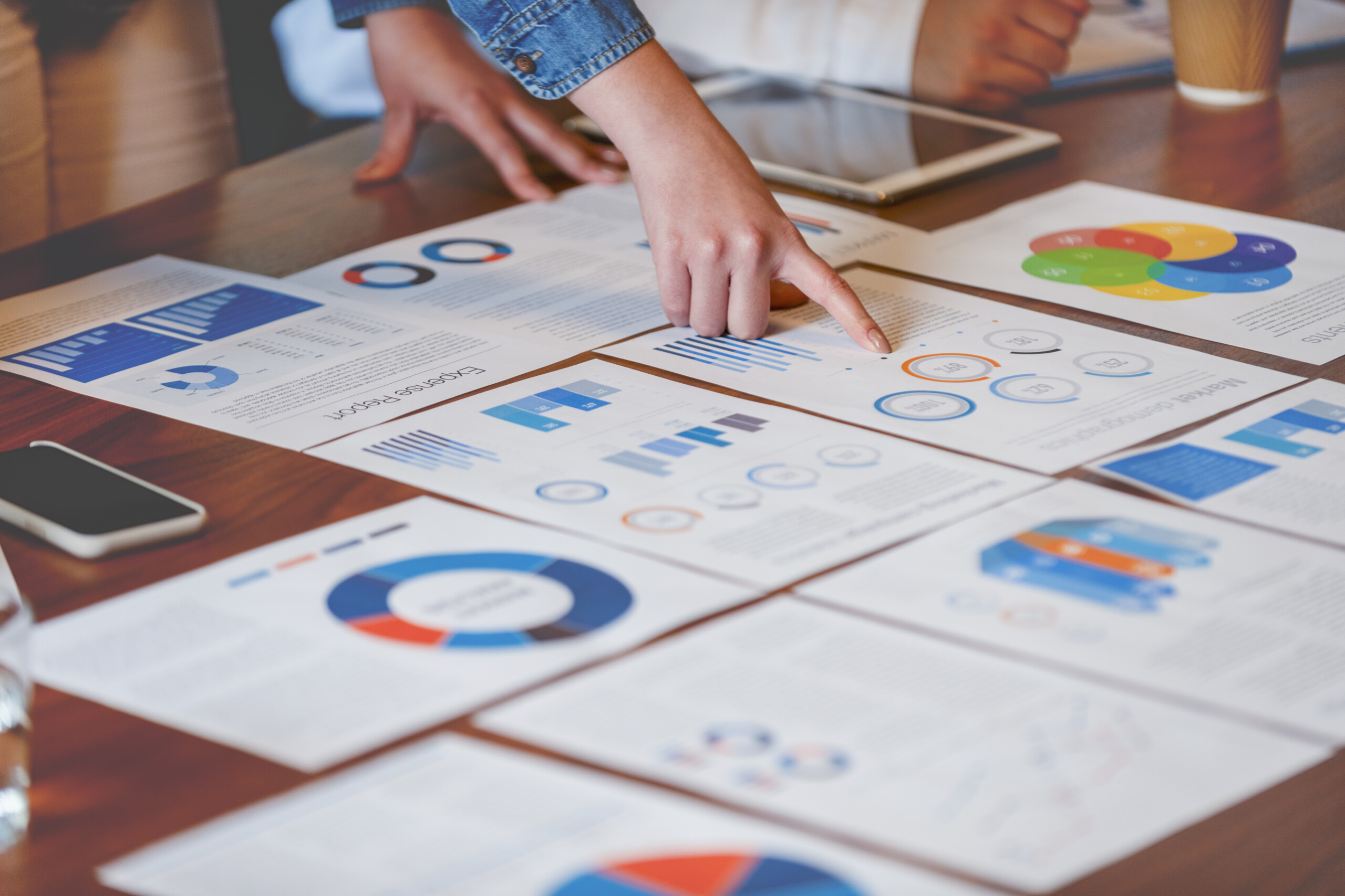 Paperwork and hands on a board room table at a business presentation or seminar. The documents have financial or marketing figures, graphs and charts on them. There...