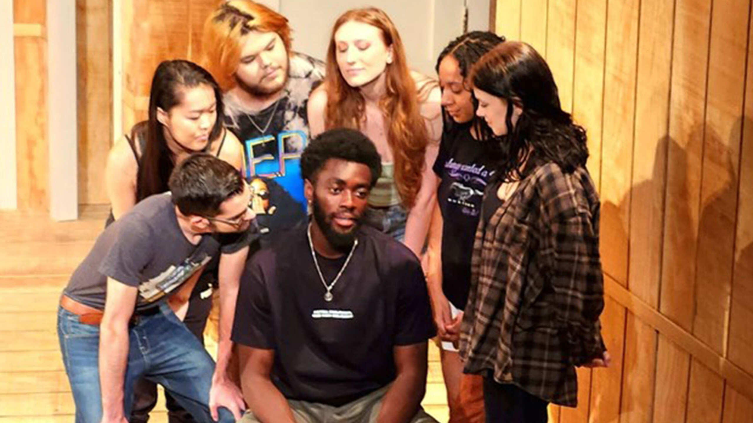 Group of people on a wooden stage with obscured faces.