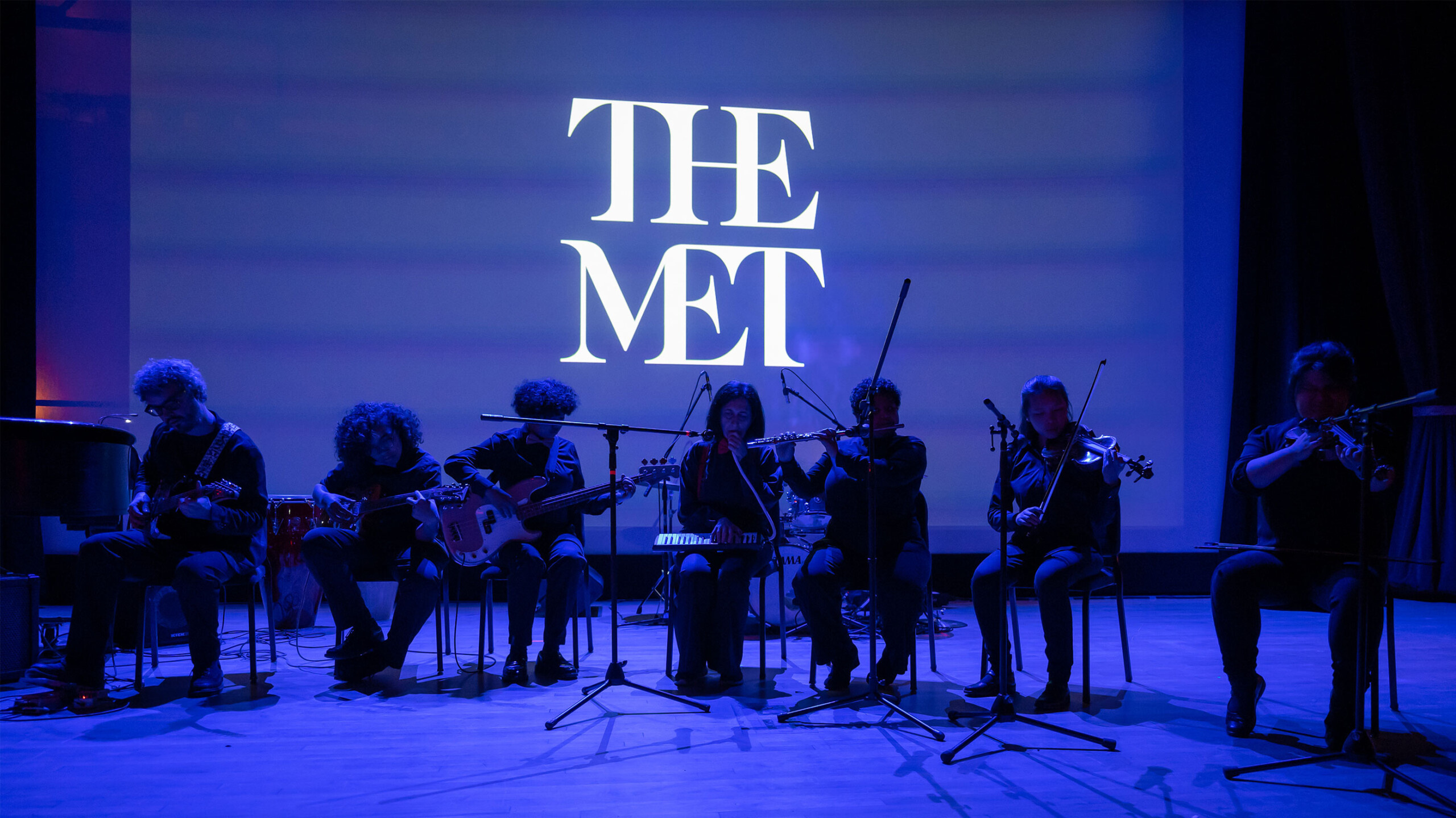A group of people dressed in black uniforms is performing on a stage. The image is set in an indoor venue, likely at a concert featuring classical music. It showcases...