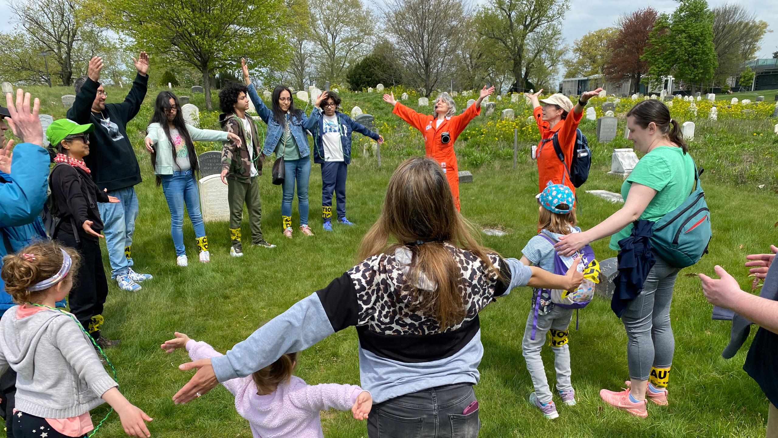 Group of people gathered in a grassy area with trees, participating in an outdoor activity.