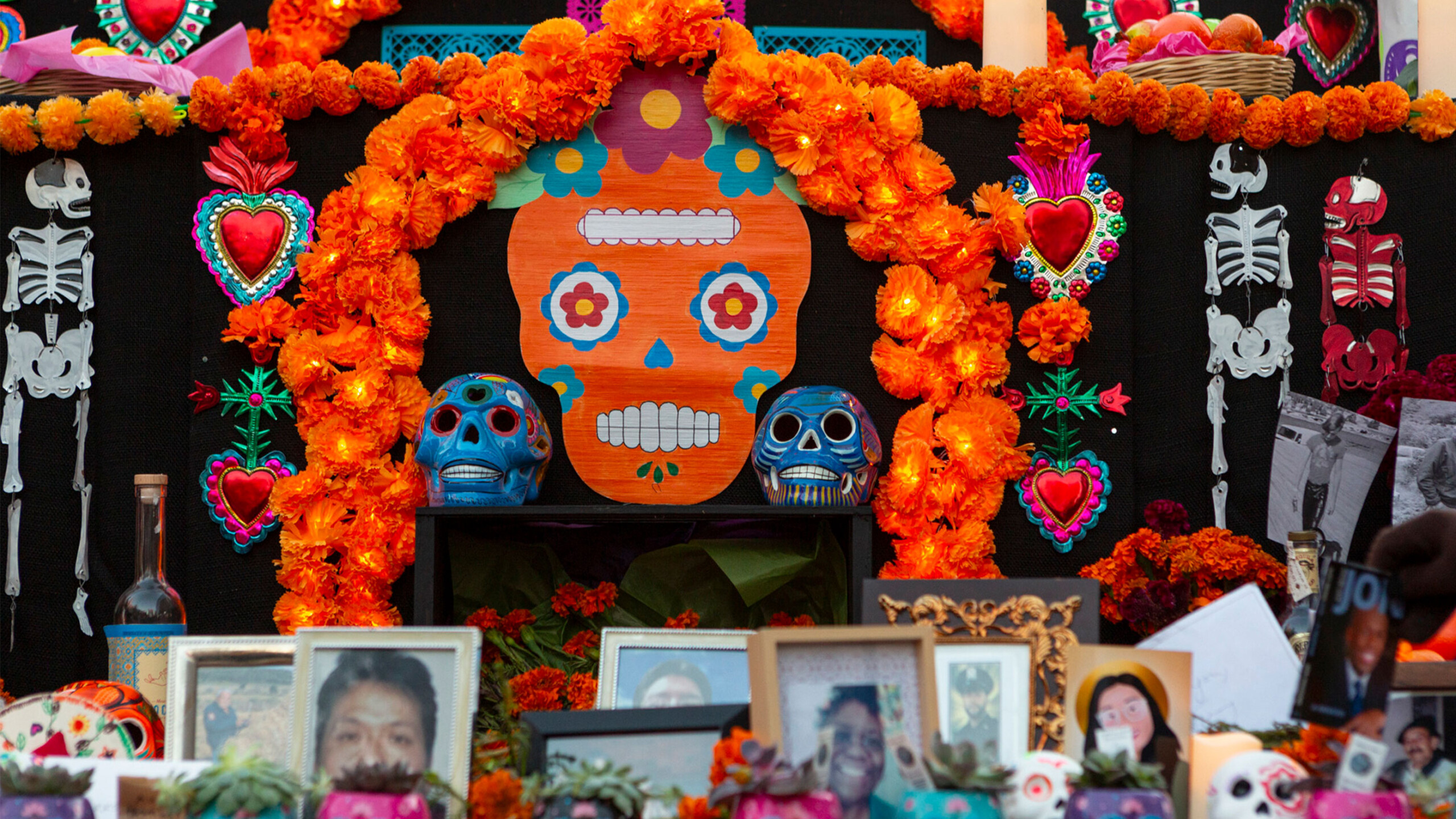 A colorful and ornate altar dedicated to the Day of the Dead, adorned with traditional marigold flowers and vibrant decorations. The centerpiece is a large paper...