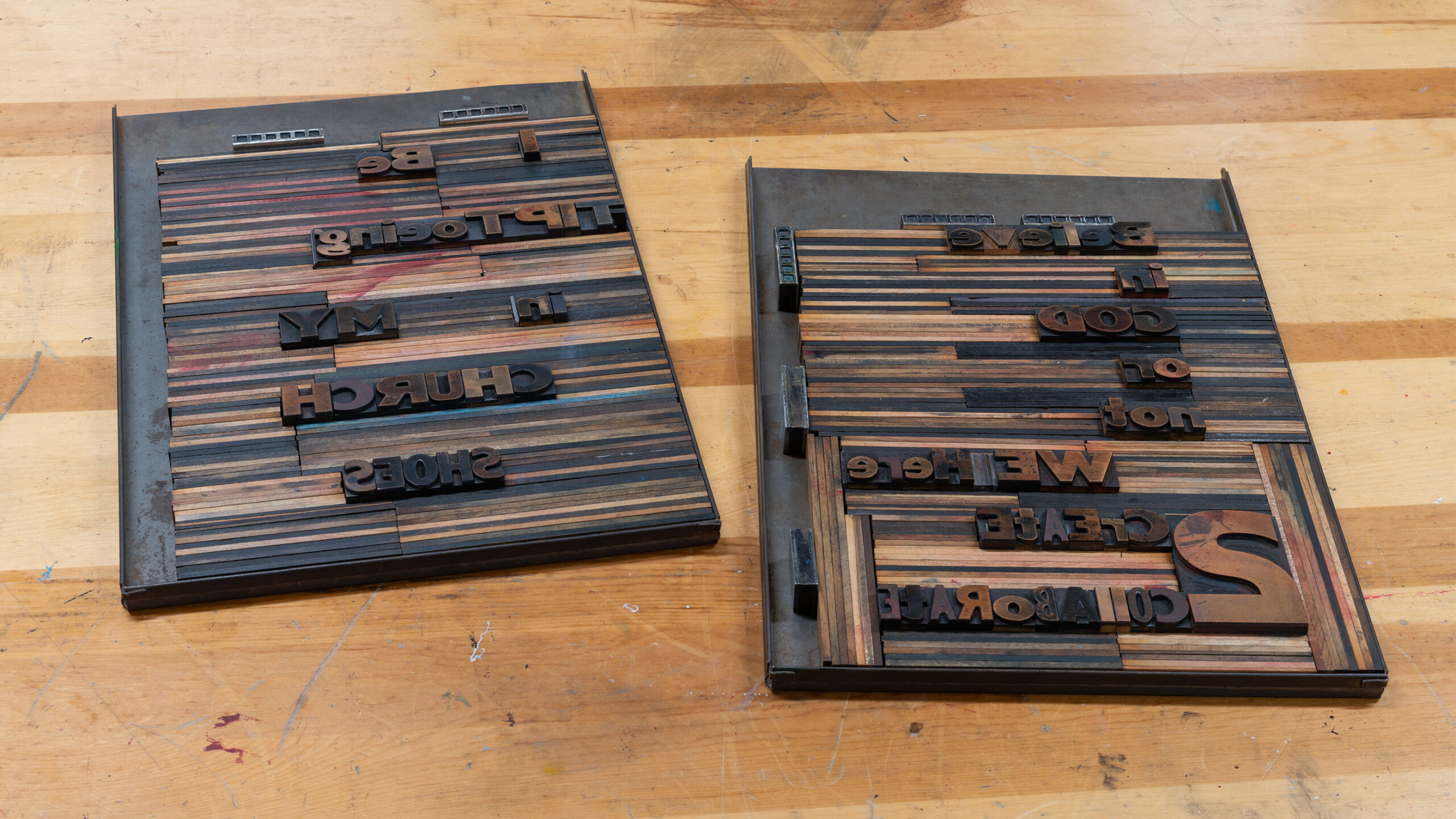 Two sets of wooden letterpress blocks are arranged side by side on a wooden surface. Each set consists of various-sized letters and spaces, creating a reversed...