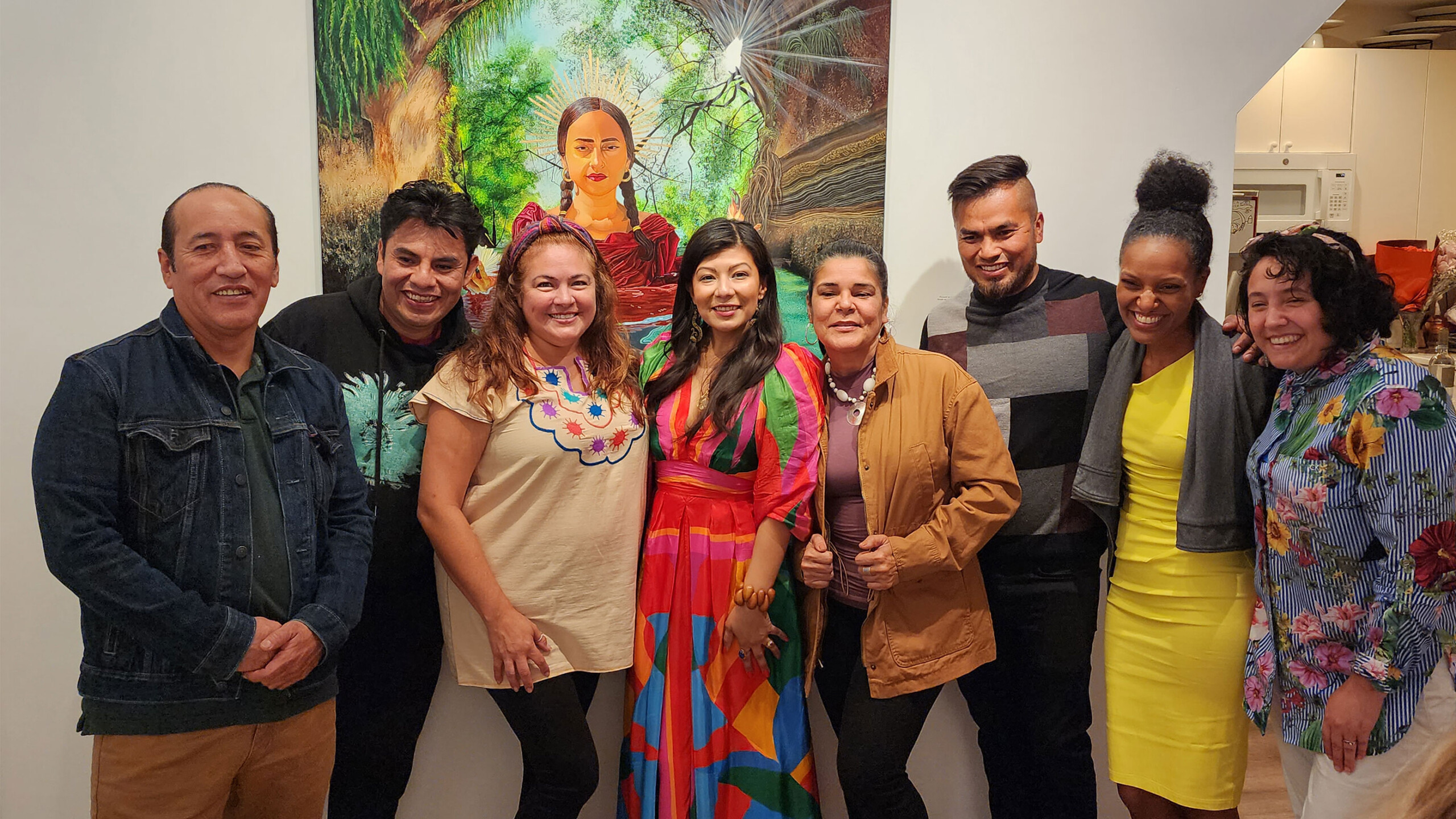 Group of people posing together indoors, with a colorful painting in the background.