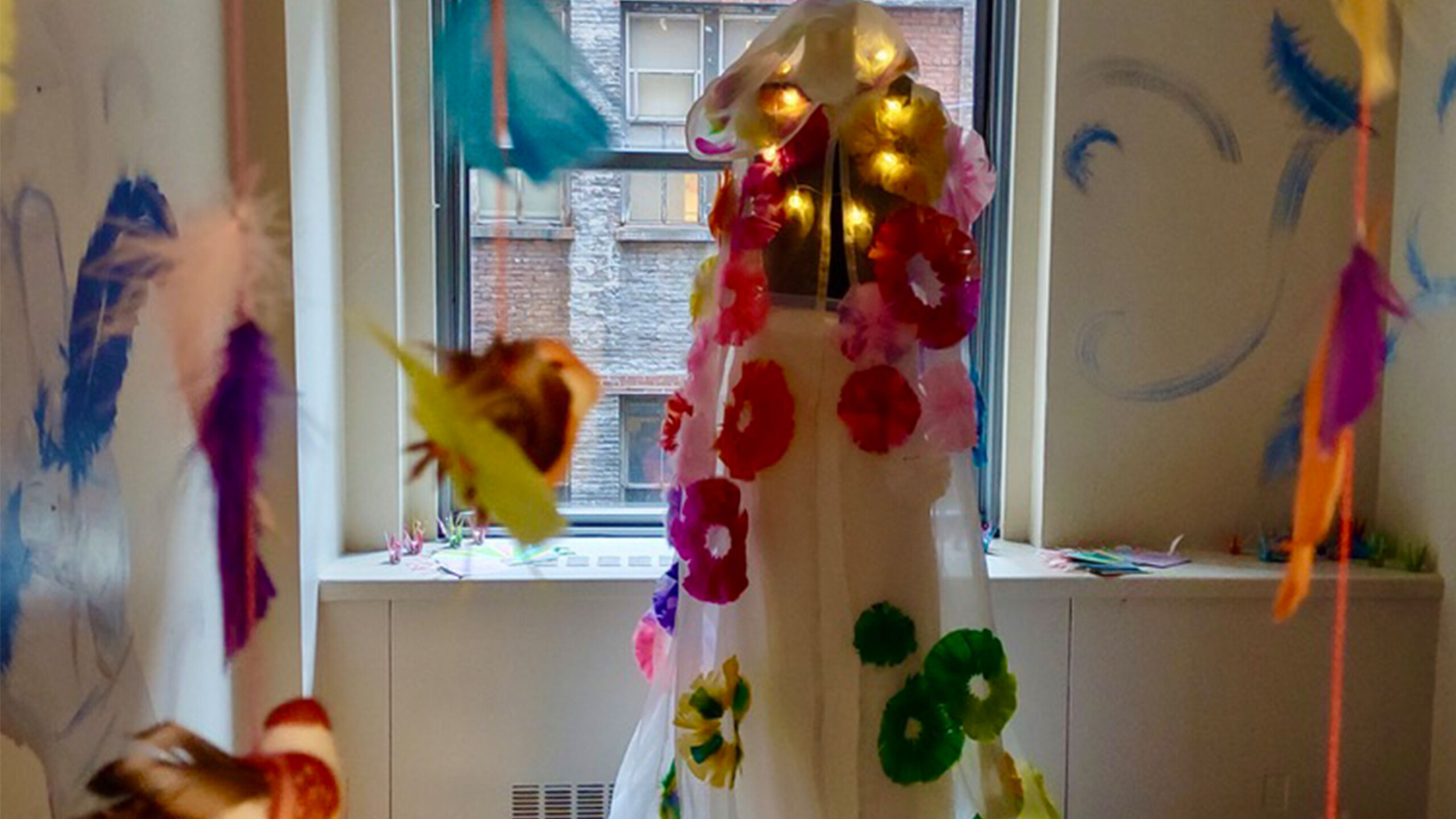 A mannequin stands adorned with a flowing, translucent fabric decorated with vibrant, large flower motifs in various colors like red, green, pink, and yellow. Surrounding...