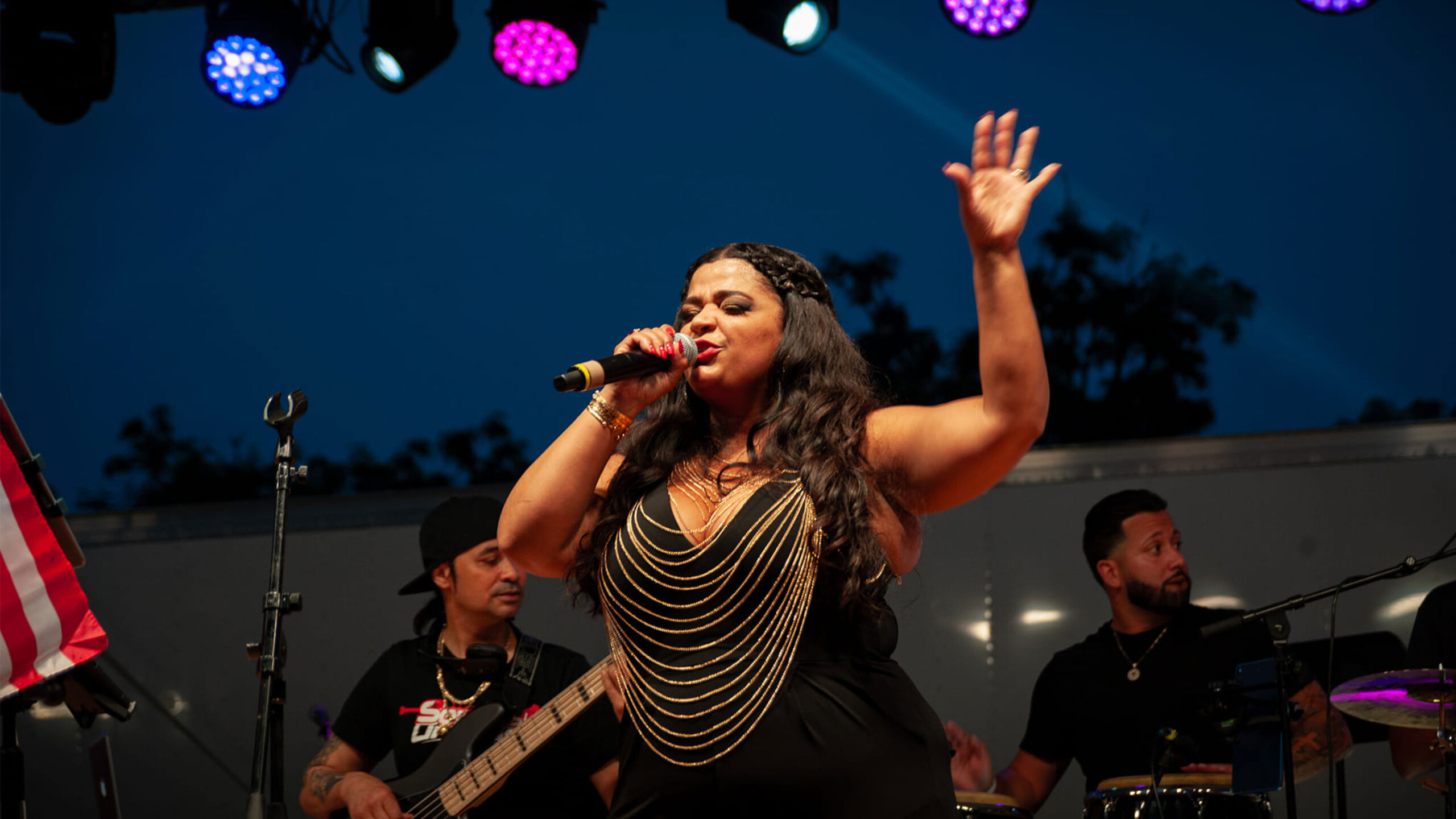 A female singer passionately performs on stage, holding a microphone with her right hand while her left hand gestures expressively in the air. She wears a black...