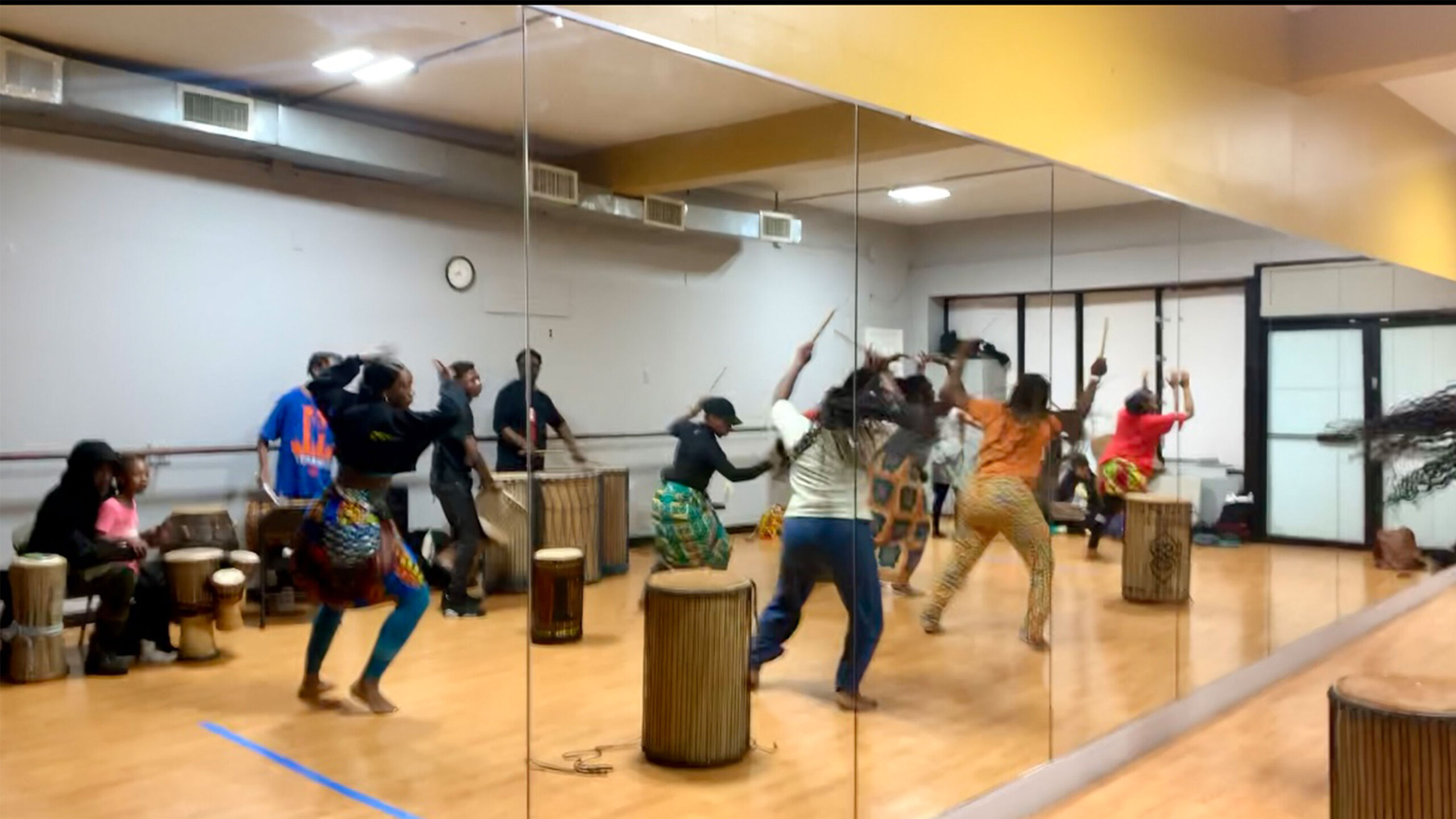 A lively dance class taking place in a mirrored dance studio. Participants are enthusiastically engaged in a dance routine, with some raised arms and energetic...