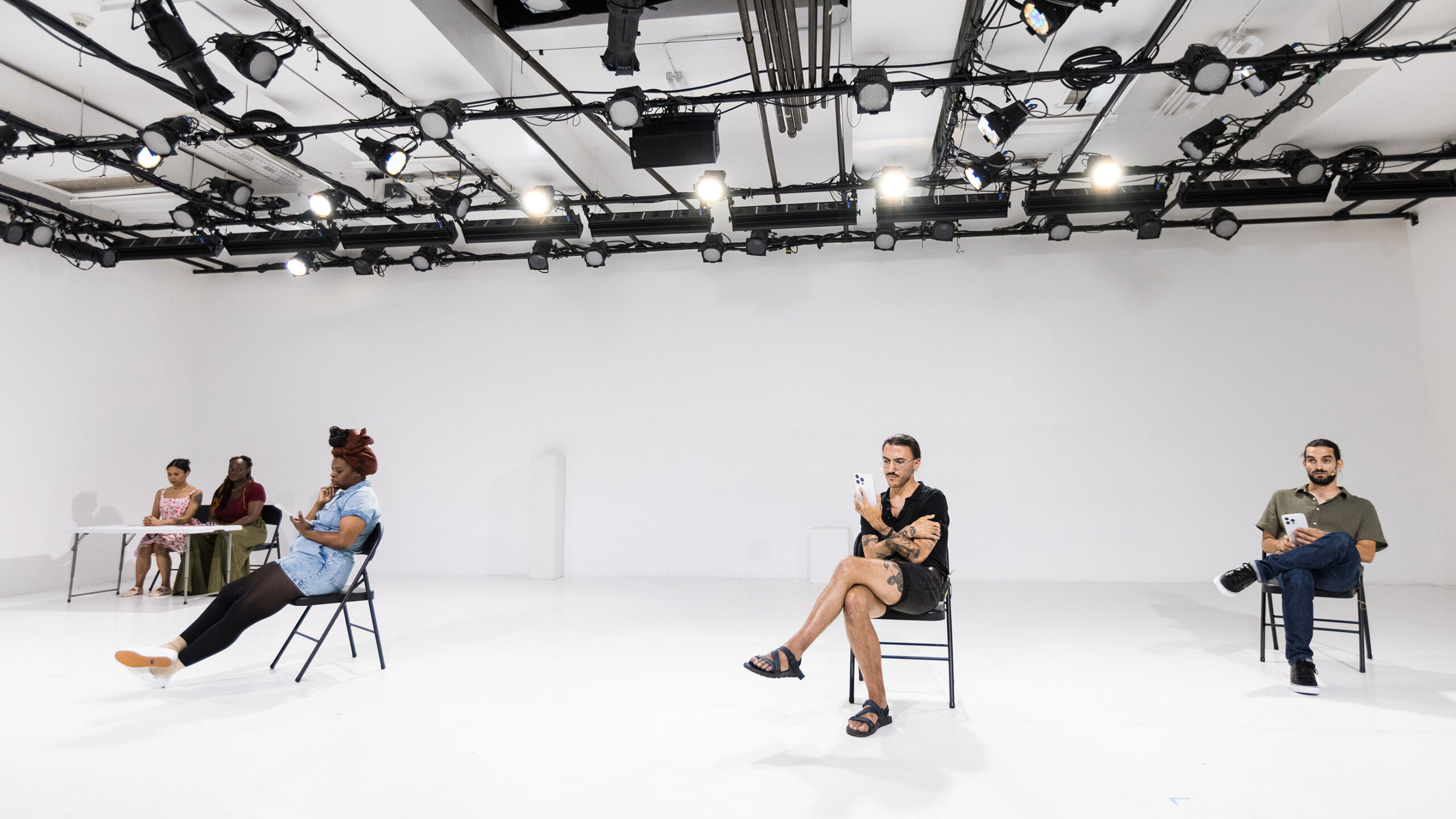 A large, white studio space equipped with an array of ceiling-mounted lights and a reflective floor creates an atmosphere of spaciousness. Three individuals, casually...