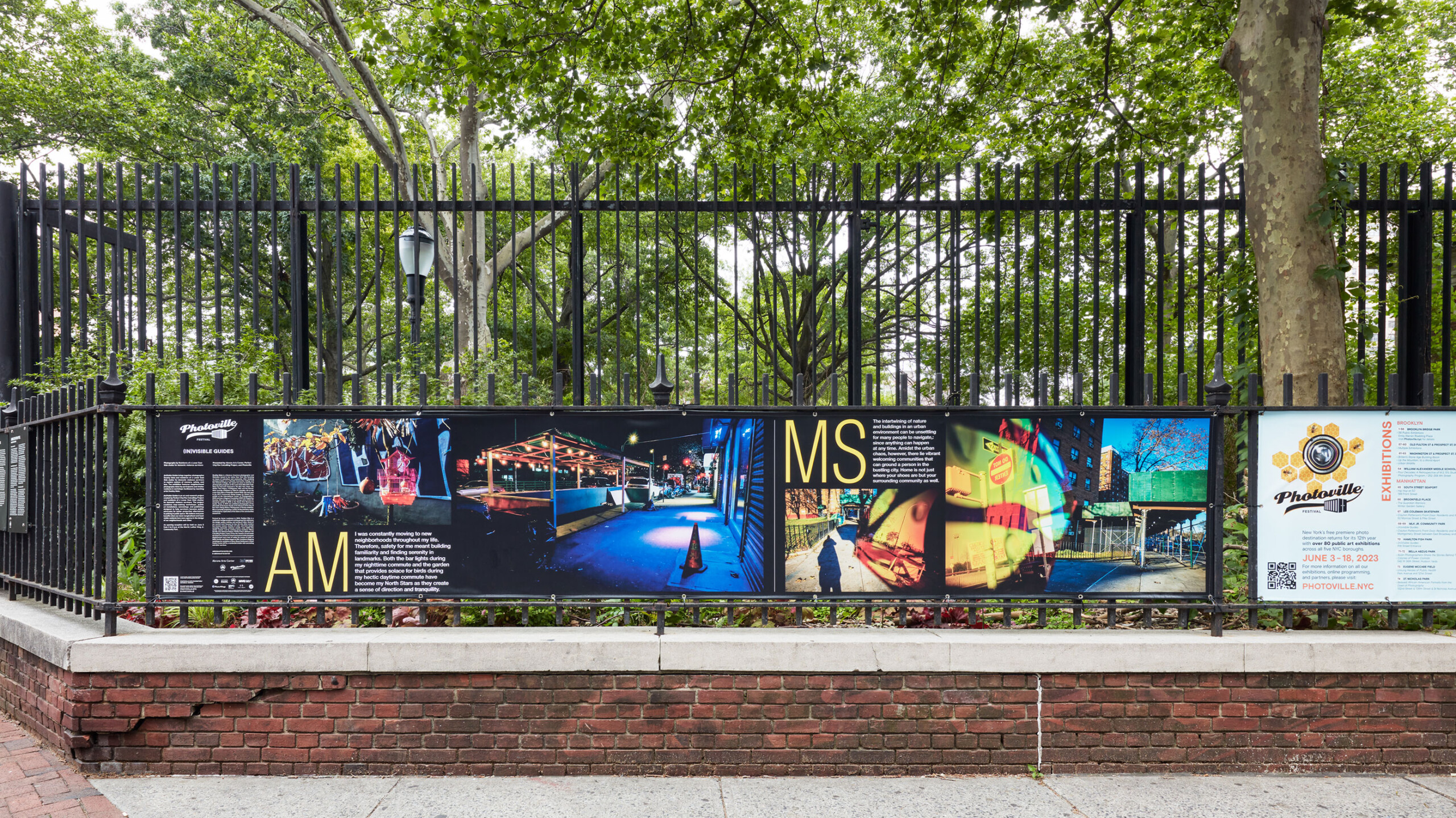 A black metal fence is adorned with a large, rectangular panel showcasing a series of vibrant images and text. The photographic content on the panel highlights...