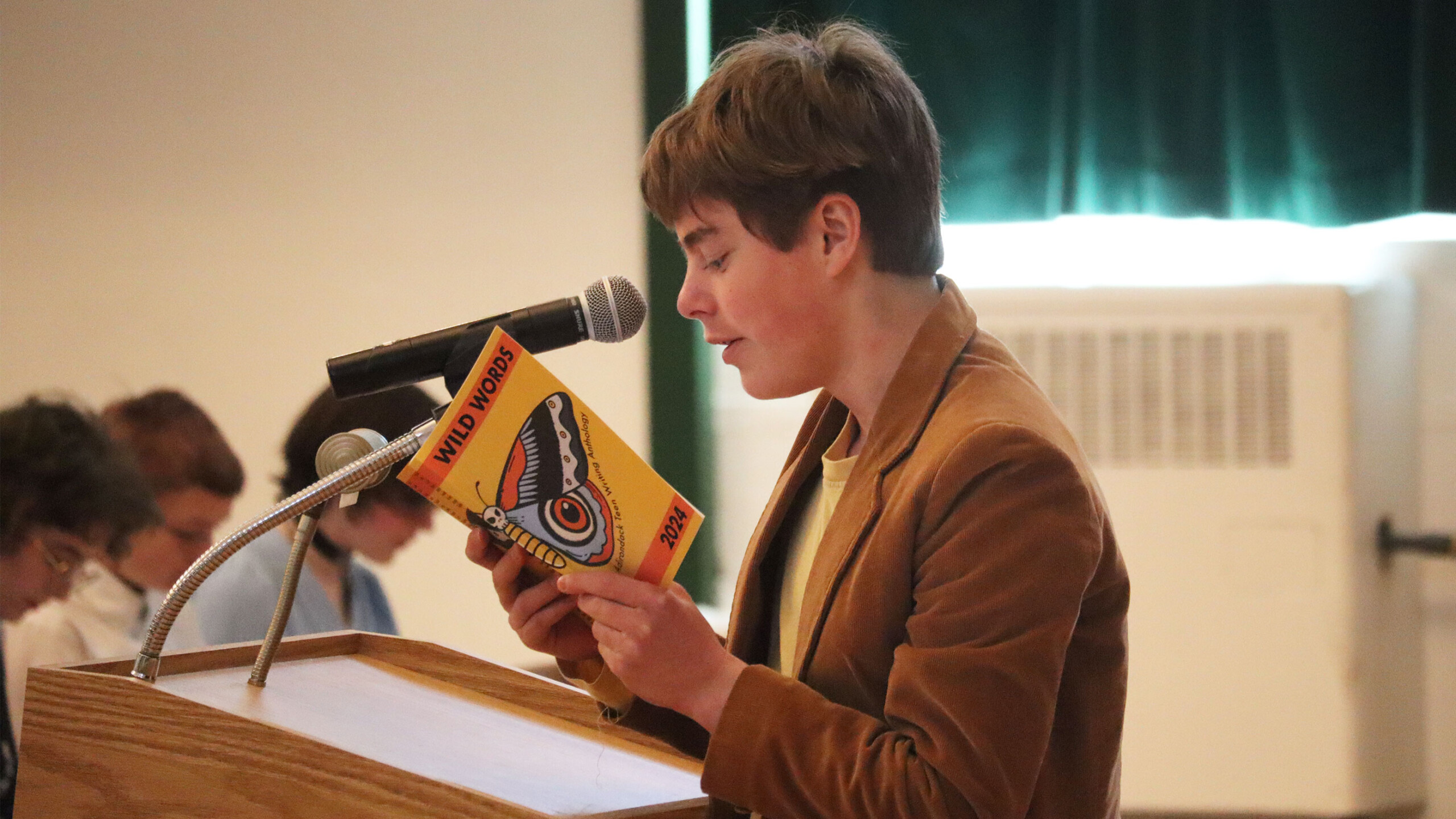 Person reading from a book at a lectern with a microphone.