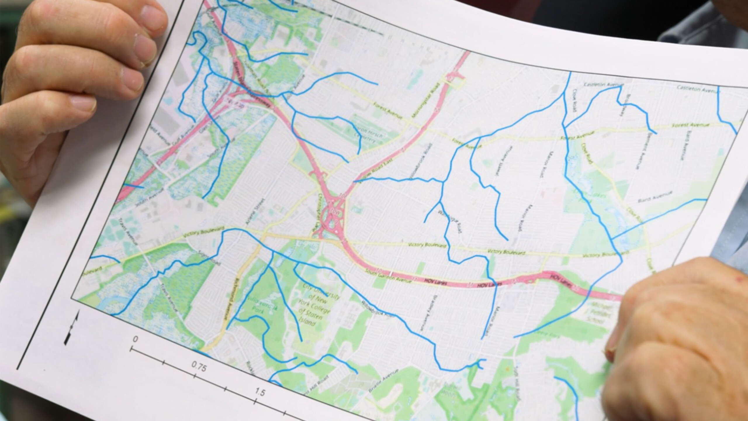 A close-up view of a person holding a printed topographical map, featuring various geographical features such as rivers, roads, and terrain. The map is oriented...