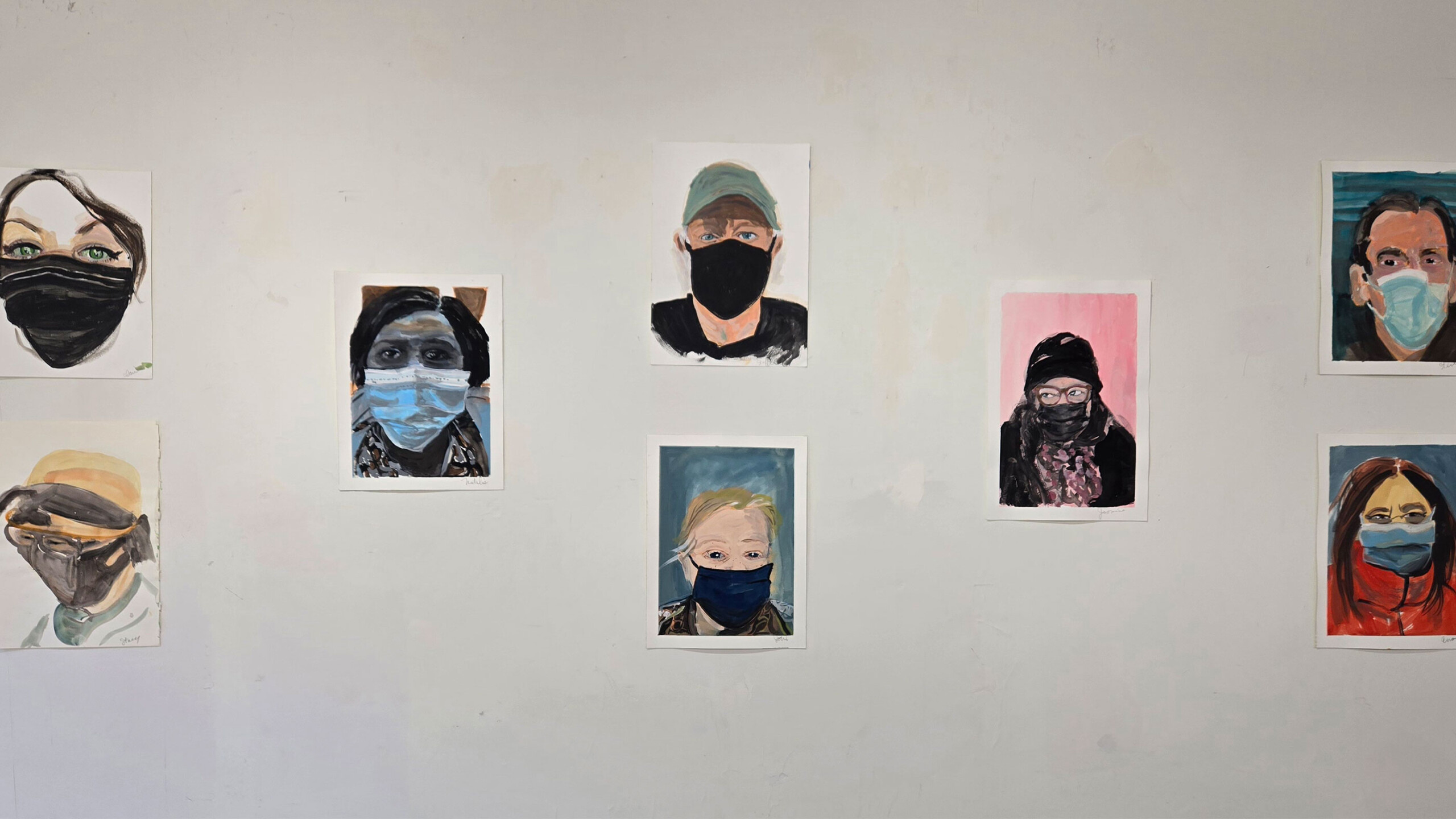 Artwork portraits on a wall with various background colors, displayed in an exhibition space.