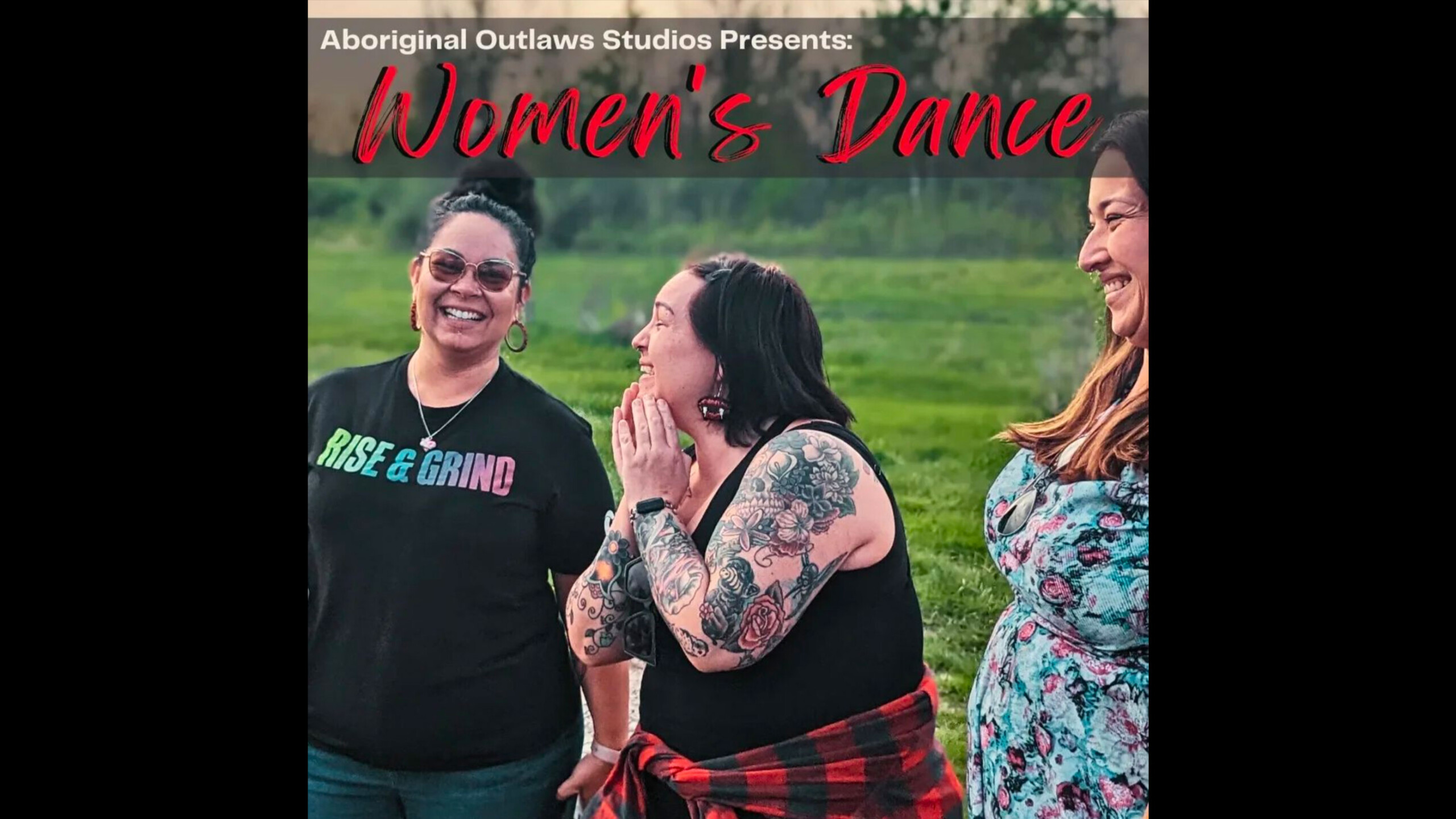 Three women standing together in a grassy outdoor setting, smiling and engaged in conversation. The woman on the left wears sunglasses, a black t-shirt with 'RISE...