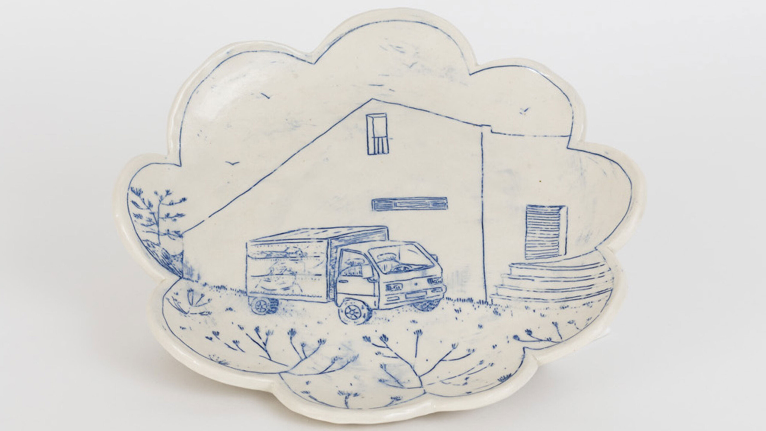 A uniquely shaped decorative plate with a scalloped edge, resembling a cloud. The plate is adorned with a blue monochrome illustration of a box truck parked in...