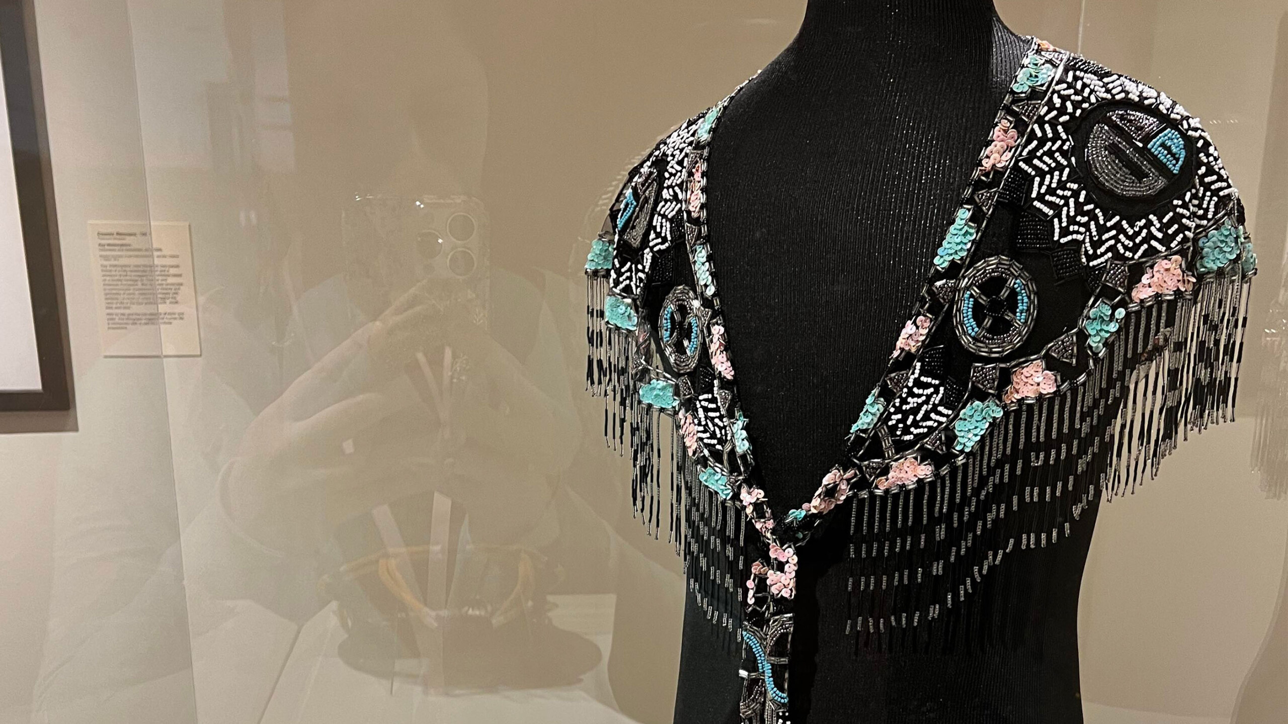 A black mannequin is adorned with an elegant beaded shawl featuring an intricate pattern. The shawl is embellished with vibrant turquoise, light pink, and white...