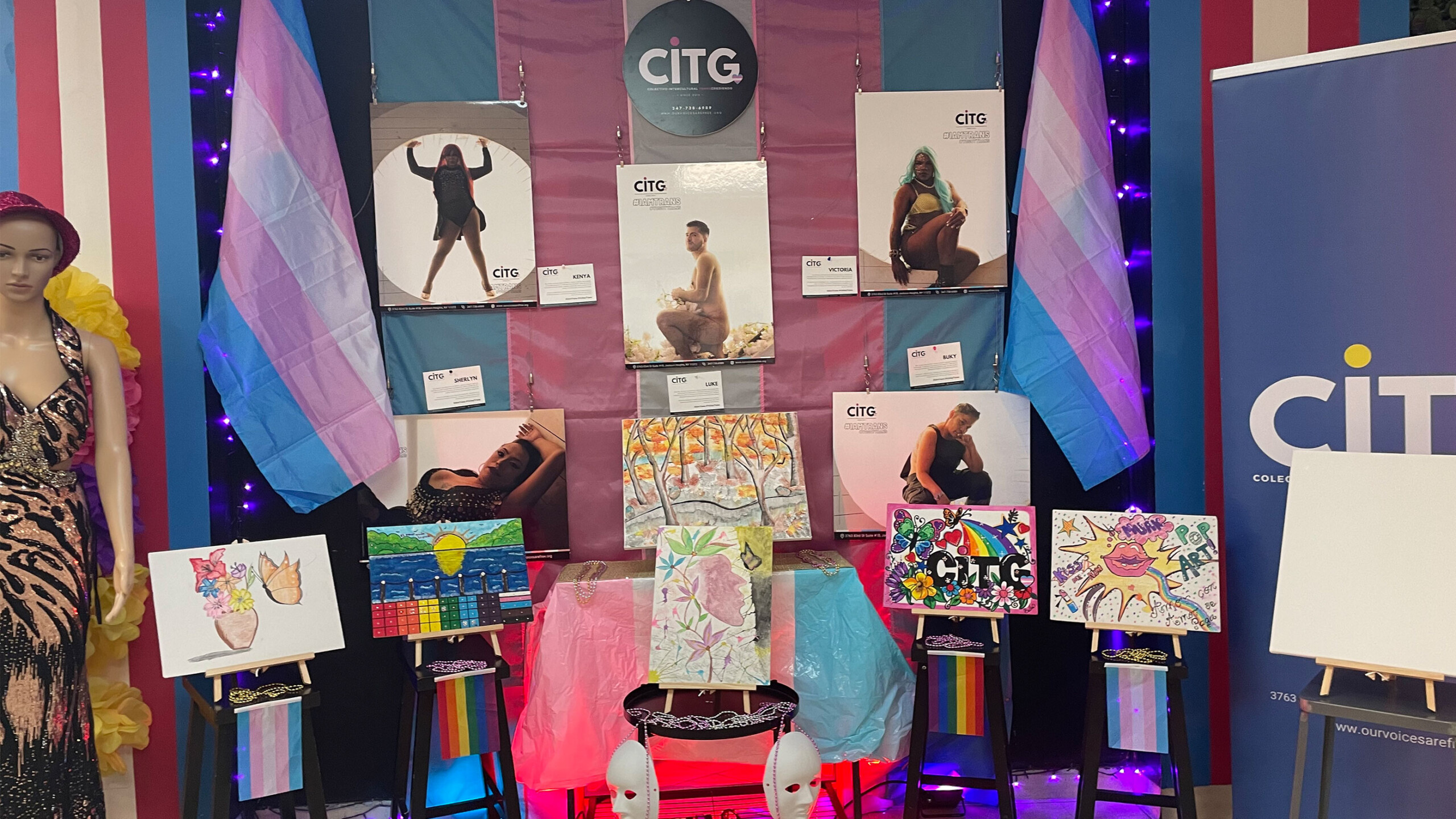 An event stand featuring colorful artwork on easels, banners, and a mannequin dressed in a sequined gown.
