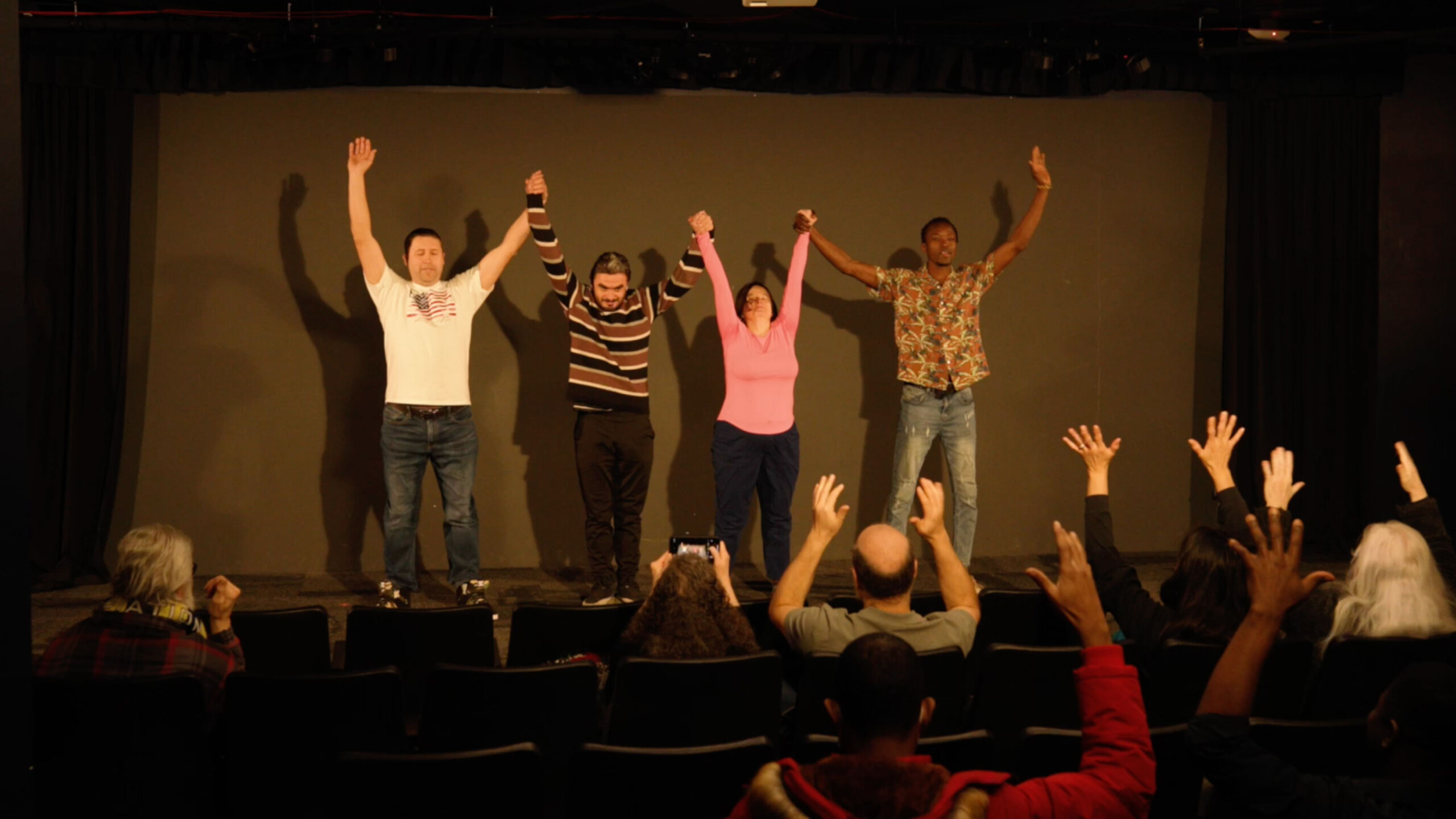 Performers on stage receiving applause from the audience in a small theater.