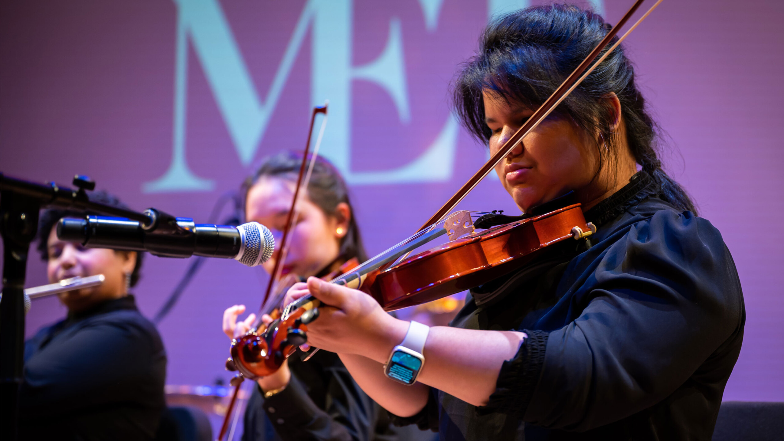 A person is playing a violin, showcasing their musical talent. The setting is likely an indoor venue, possibly during a recital or concert. The performance highlights...