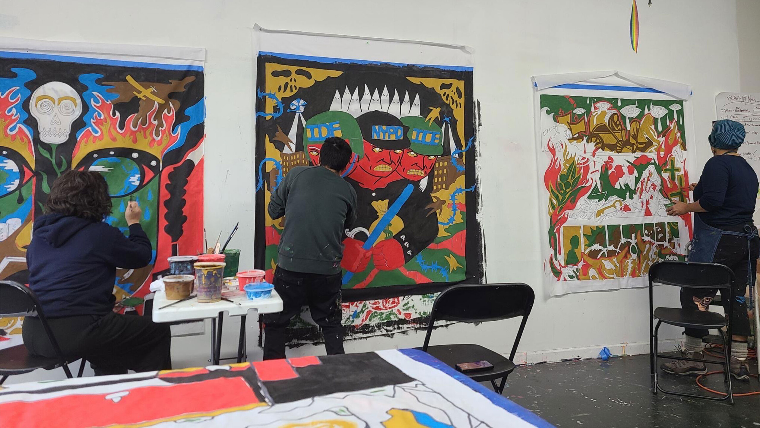 Artists painting colorful, large-scale canvases with bold graphics in a studio setting.
