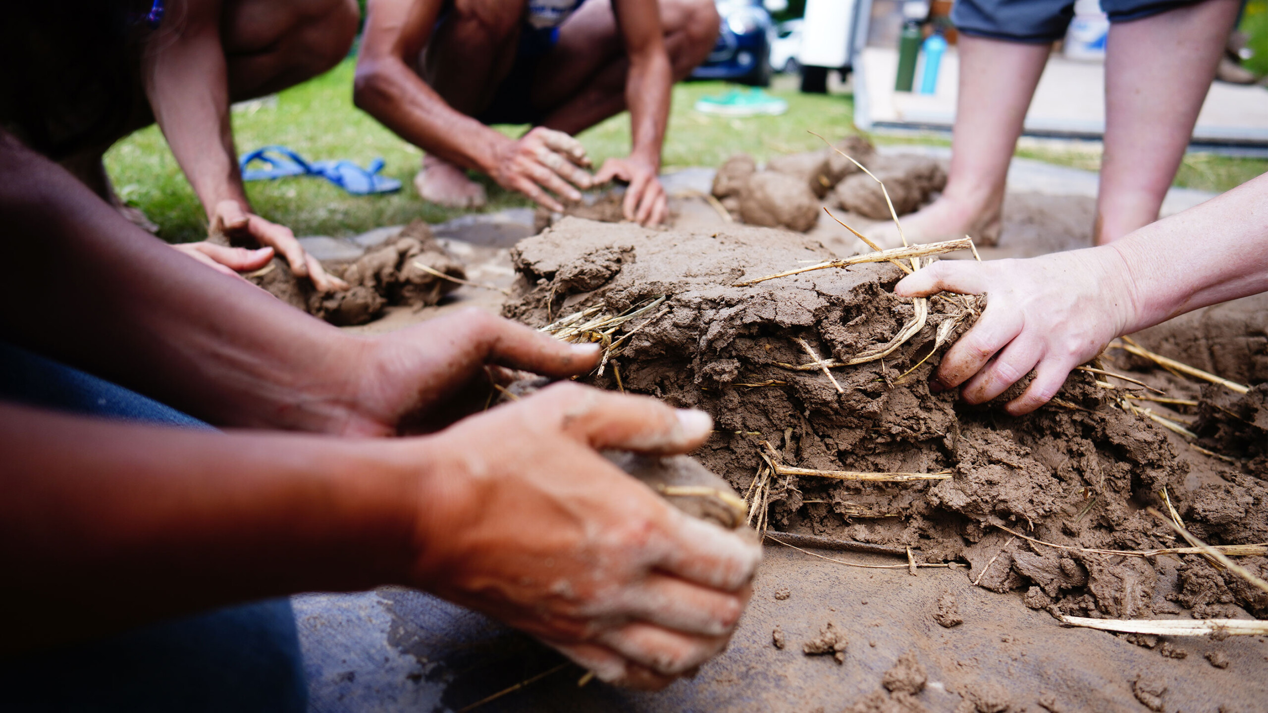 A group of people is collaborating on creating a sand sculpture. They are working outdoors, cutting and shaping the sand with various tools. The scene captures...