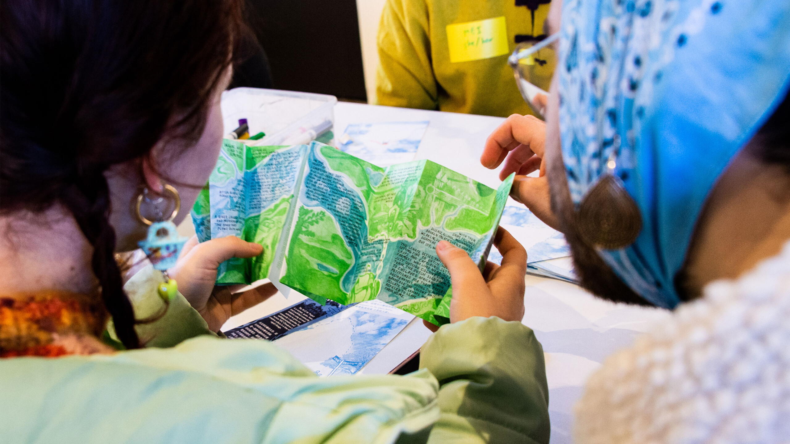 Two individuals are closely examining a folded map with vibrant green and blue areas, likely representing geographic features such as forests or parks and bodies...