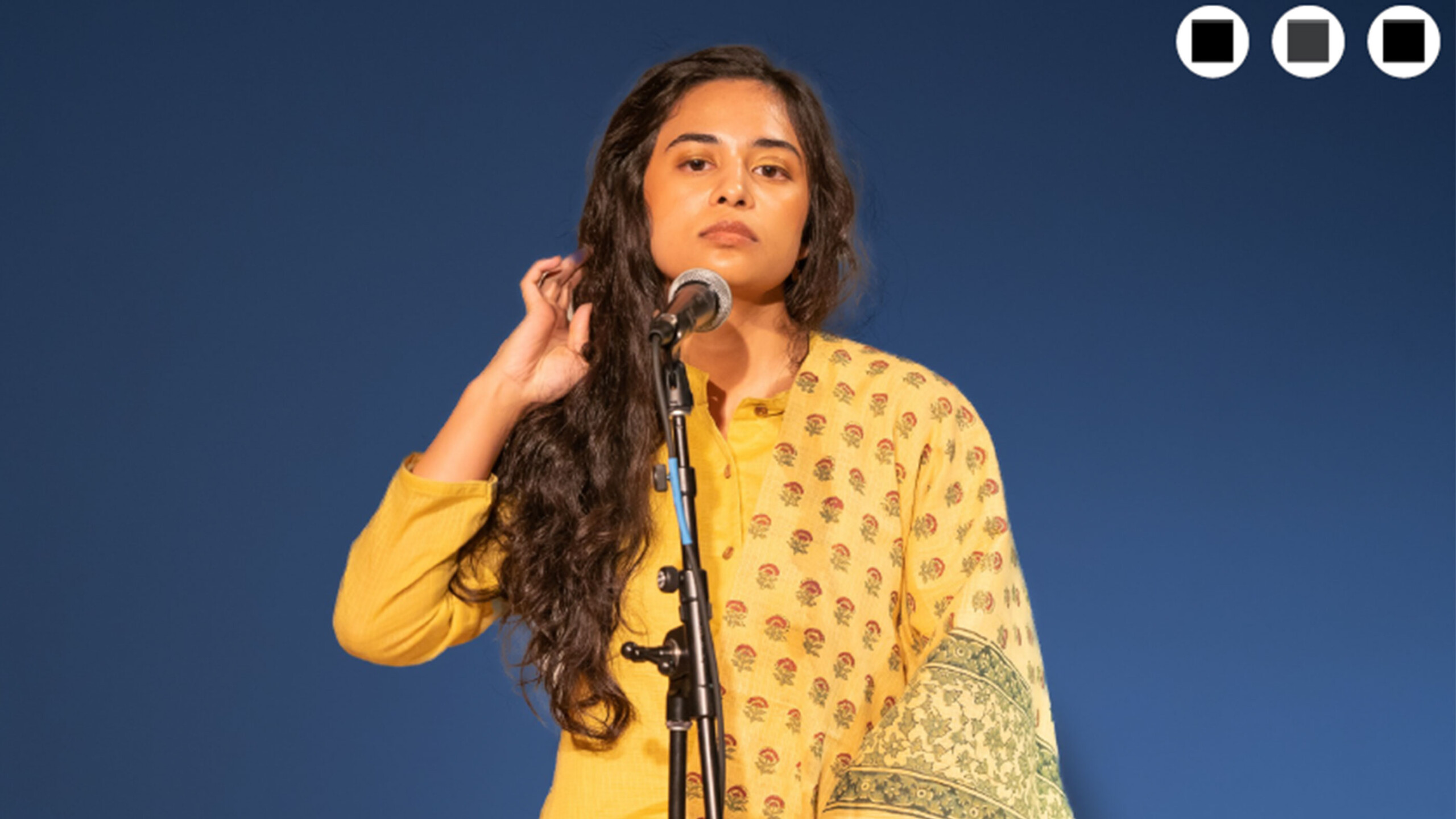 Person in yellow attire speaking into a microphone on stage.