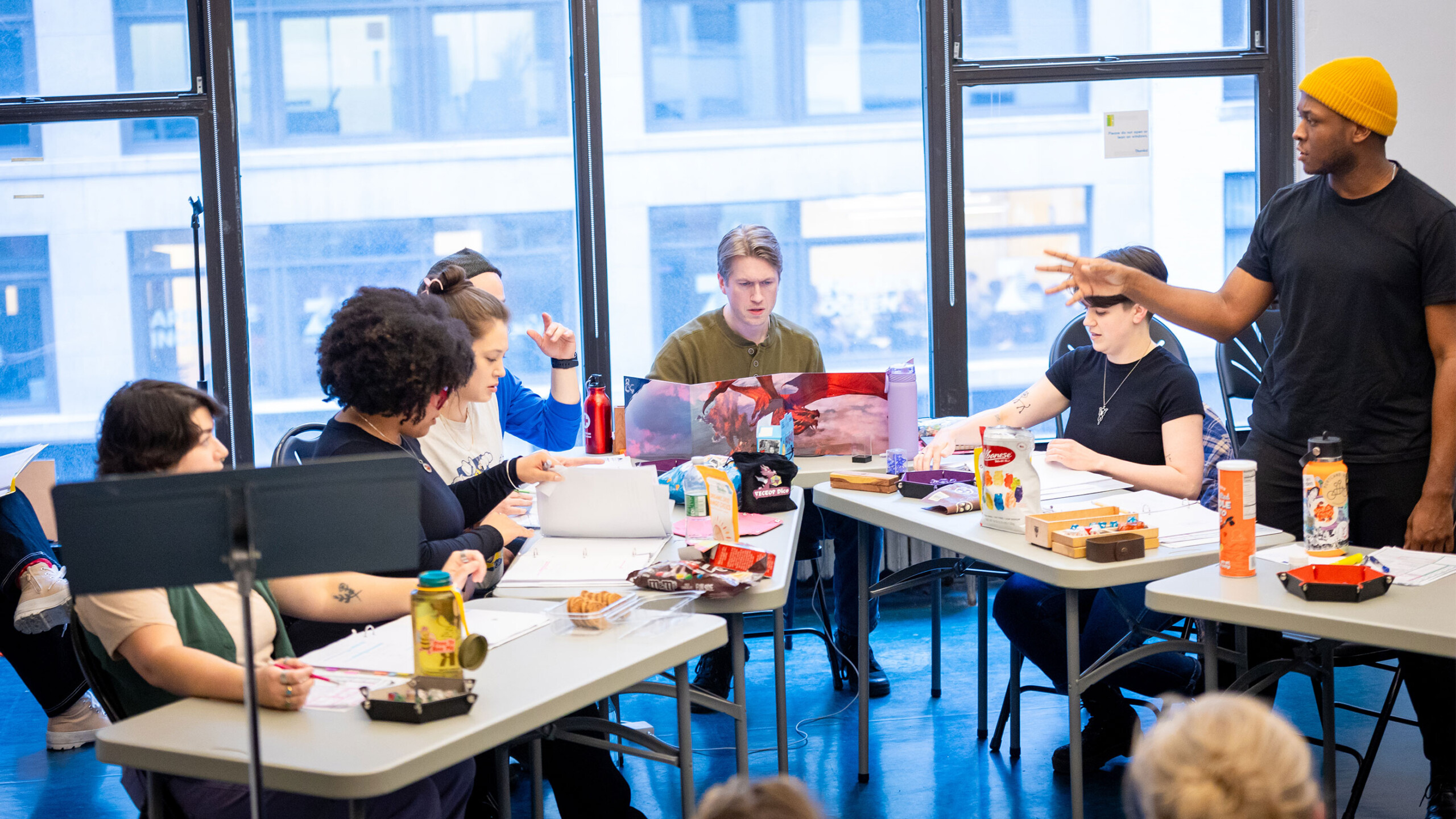 A group of people engaging in a creative workshop with laptops and art supplies on tables.