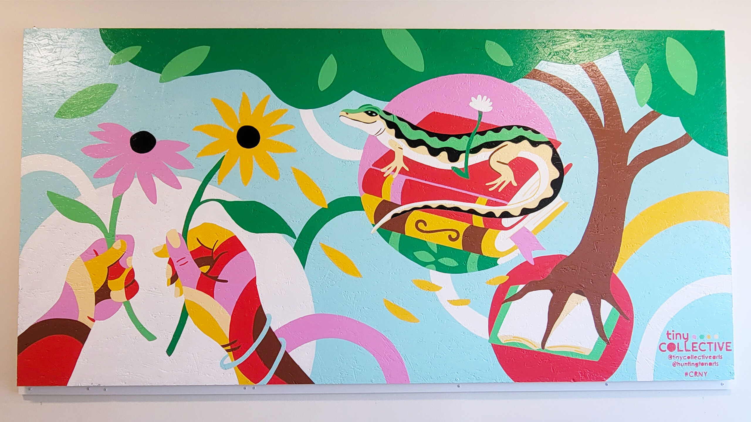 A colorful mural featuring a stylized, graphic design of nature themes. Two hands, painted in shades of pink, red, and yellow, extend into the scene, each holding...