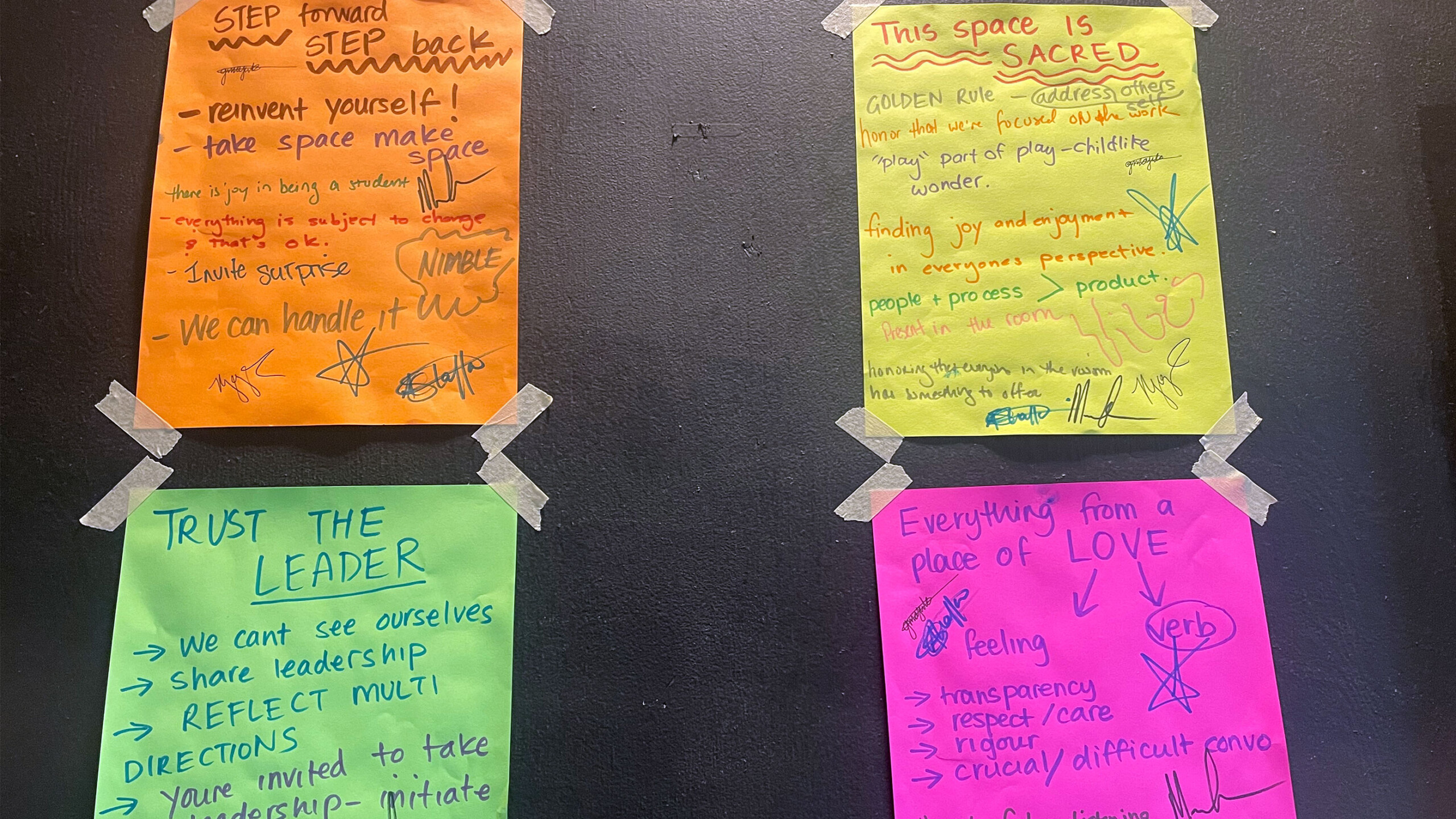 Four brightly colored Post-it notes are taped onto a dark surface, each displaying various handwritten messages and guidelines. The notes are in orange, yellow,...