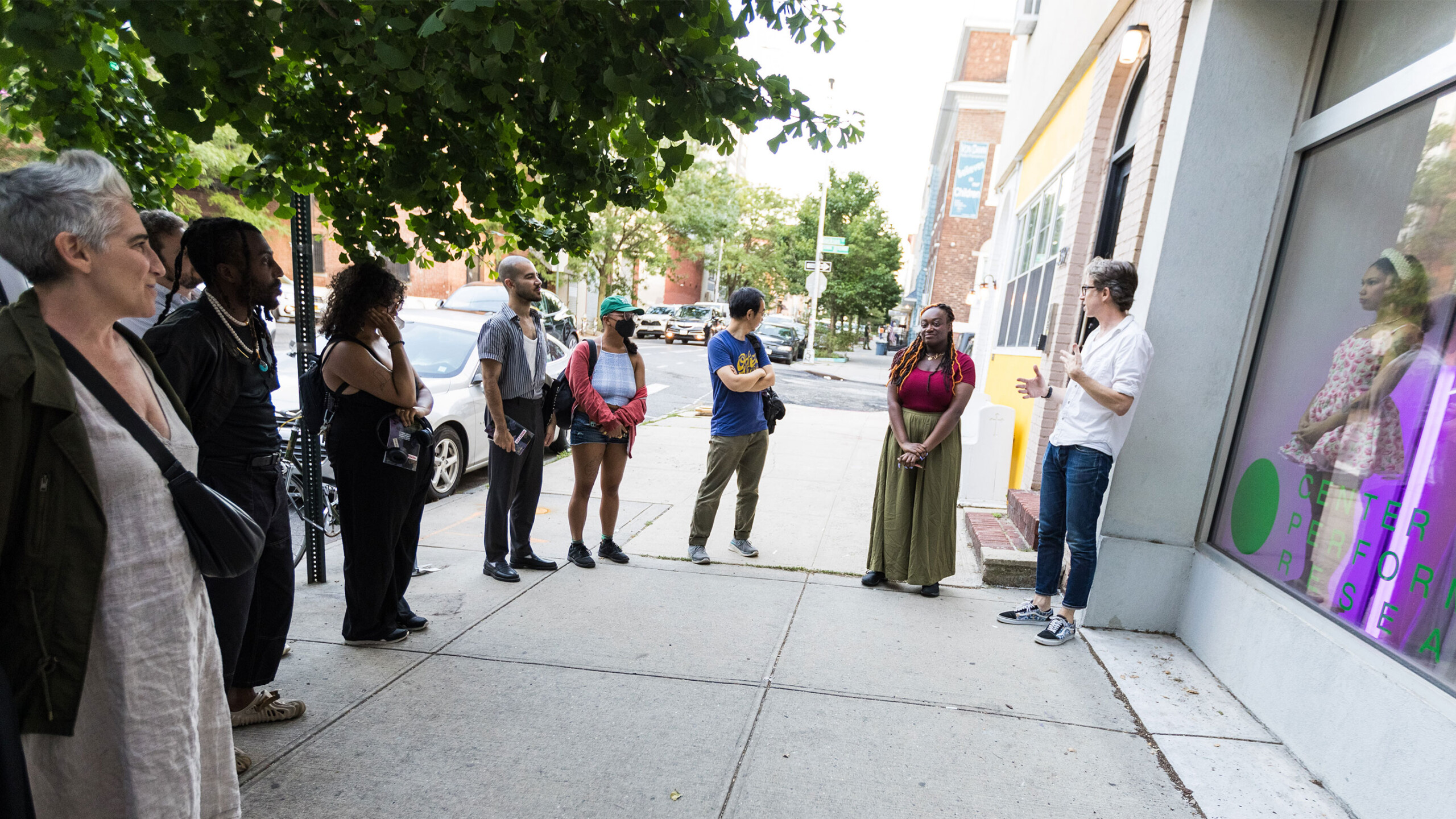 A group of people standing on a sidewalk in front of a building.