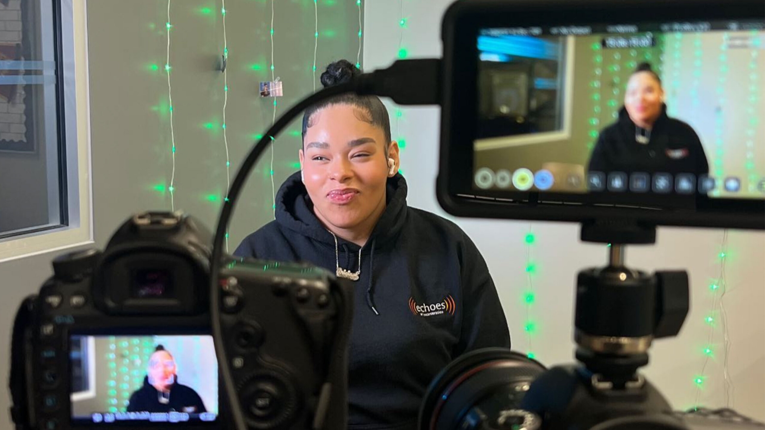 The image shows a person sitting behind a camera. The person appears to be in an indoor setting, possibly working in the television or media industry. There is...