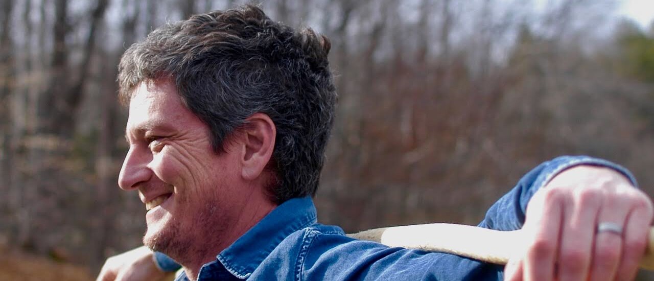 Photo of Andrew Simonet standing outdoors in a blue longsleeve shirt smiling.
