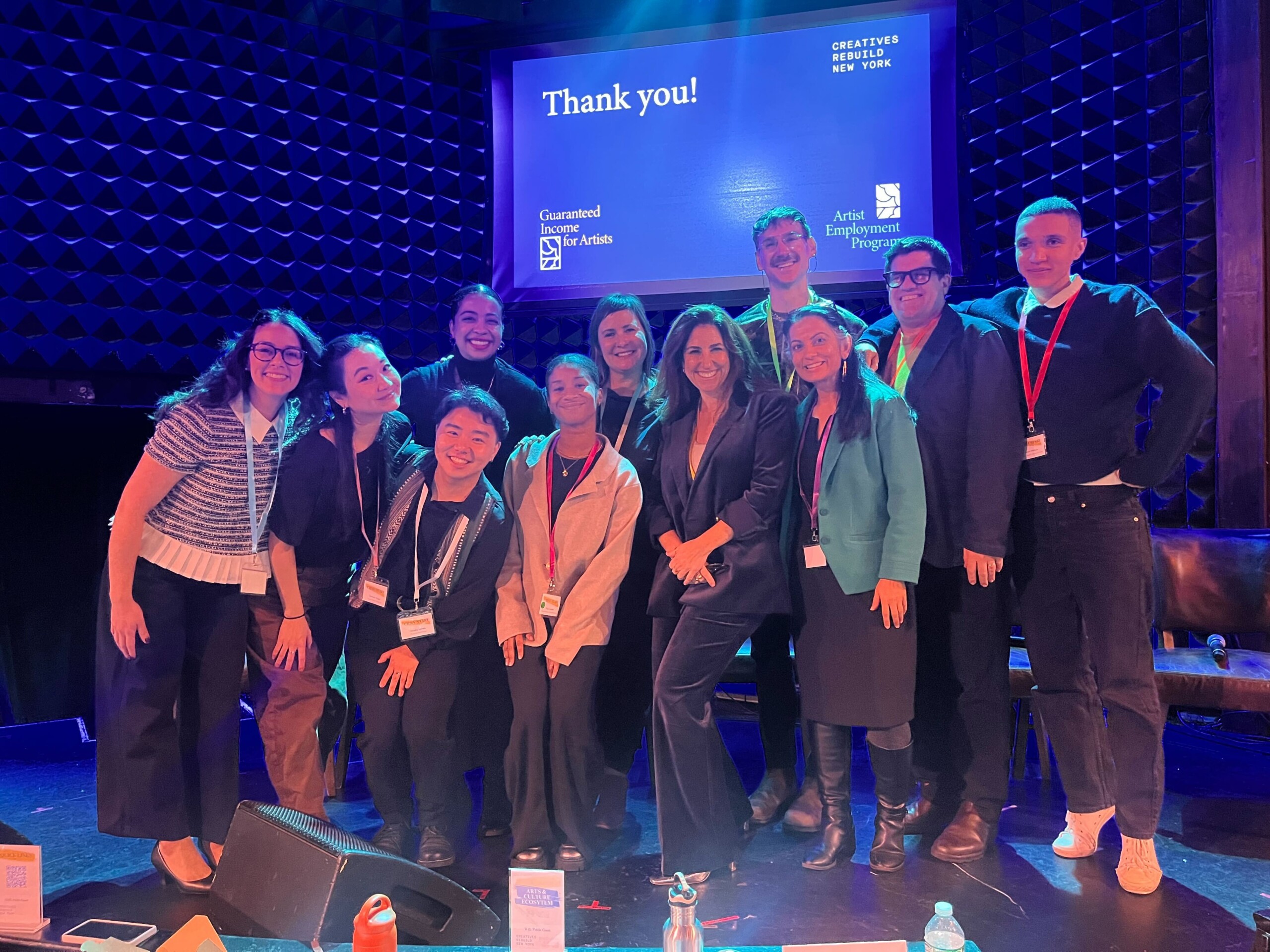 A group photo of the CRNY staff on a stage, smiling widely for a camera just to the left.